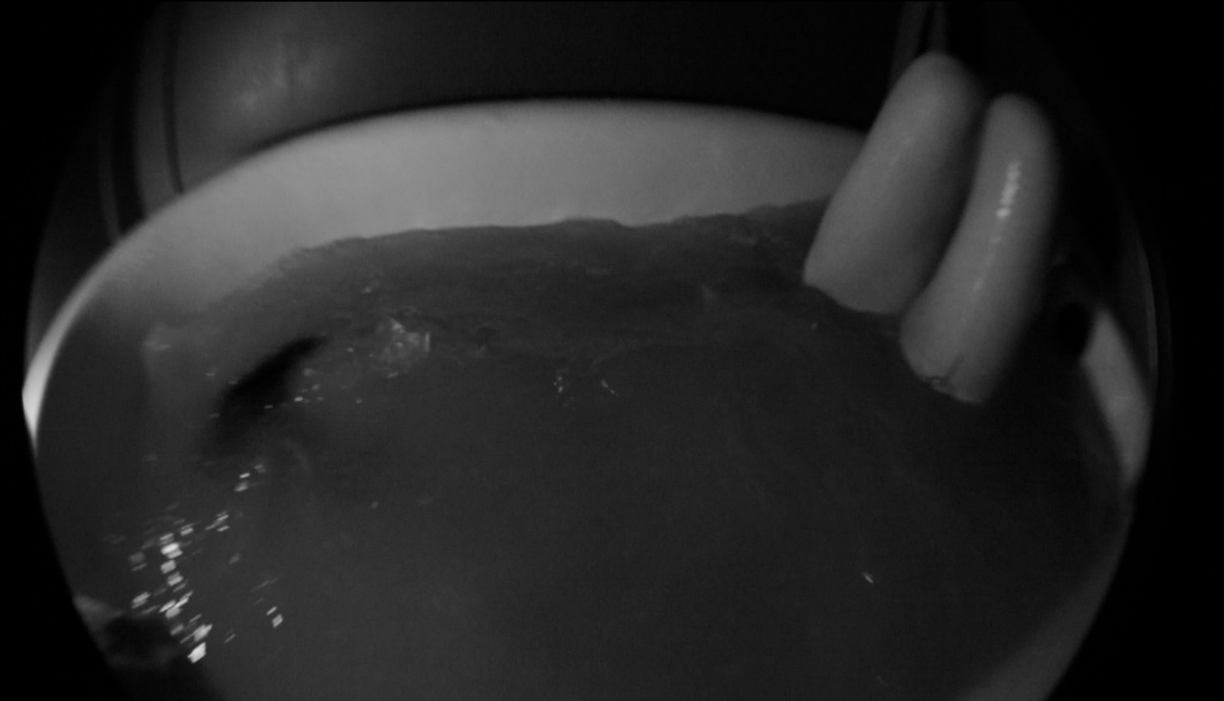 A hand holding a cup of dark liquid, possibly coffee or tea, viewed through a circular opening or on a round reflective surface.