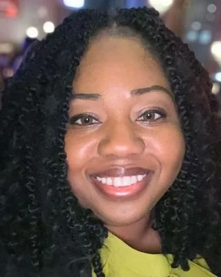 A woman with dark, curly hair wearing a green top and smiling for the camera.