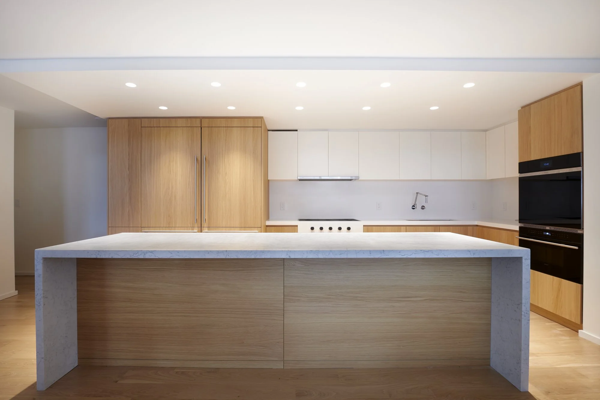 Modern kitchen with wooden cabinets, white upper cabinets, and a large island with a marble countertop.