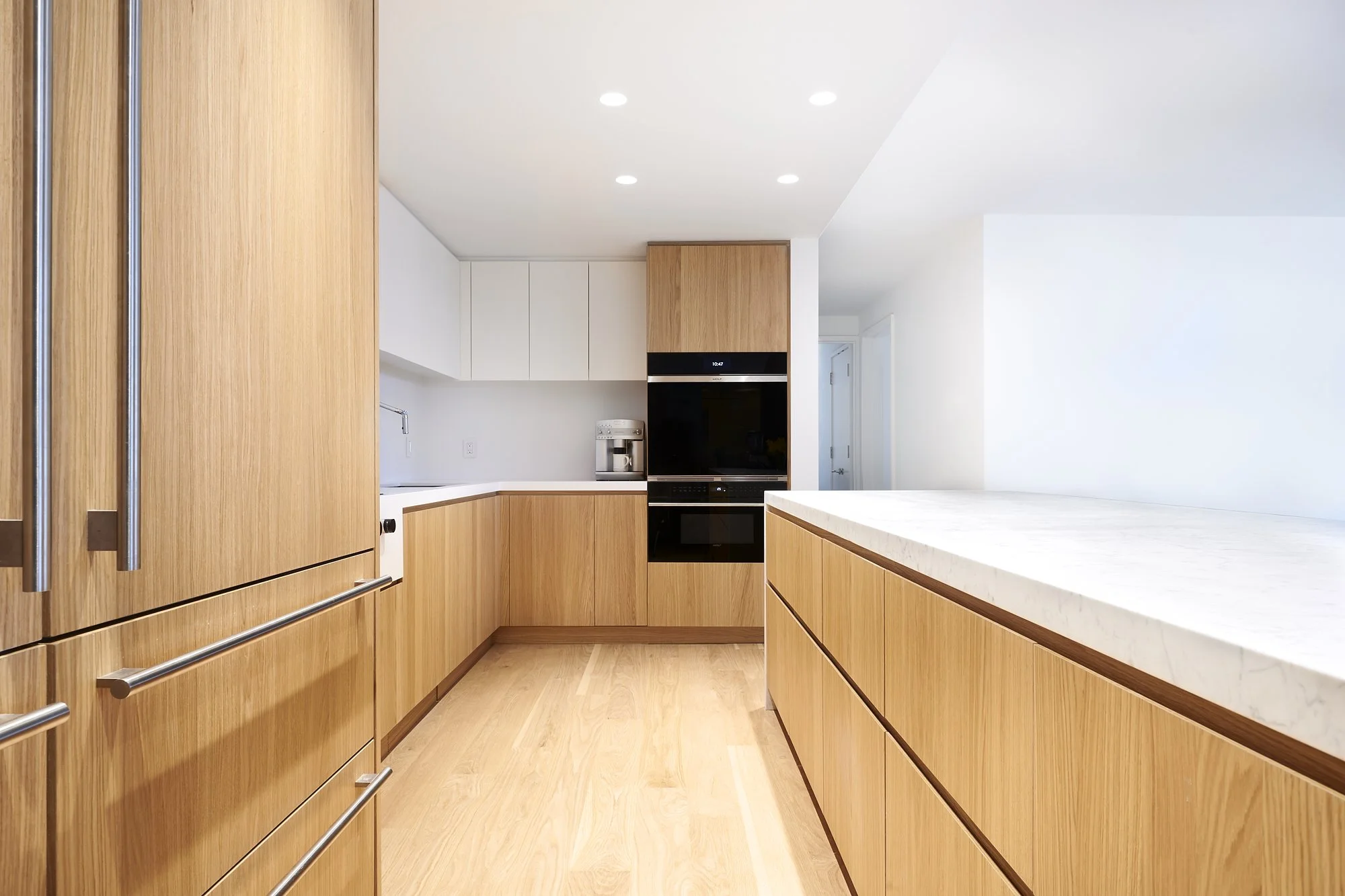 Modern kitchen with wooden cabinets, white countertops, built-in black oven and microwave, and a coffee maker on the counter.