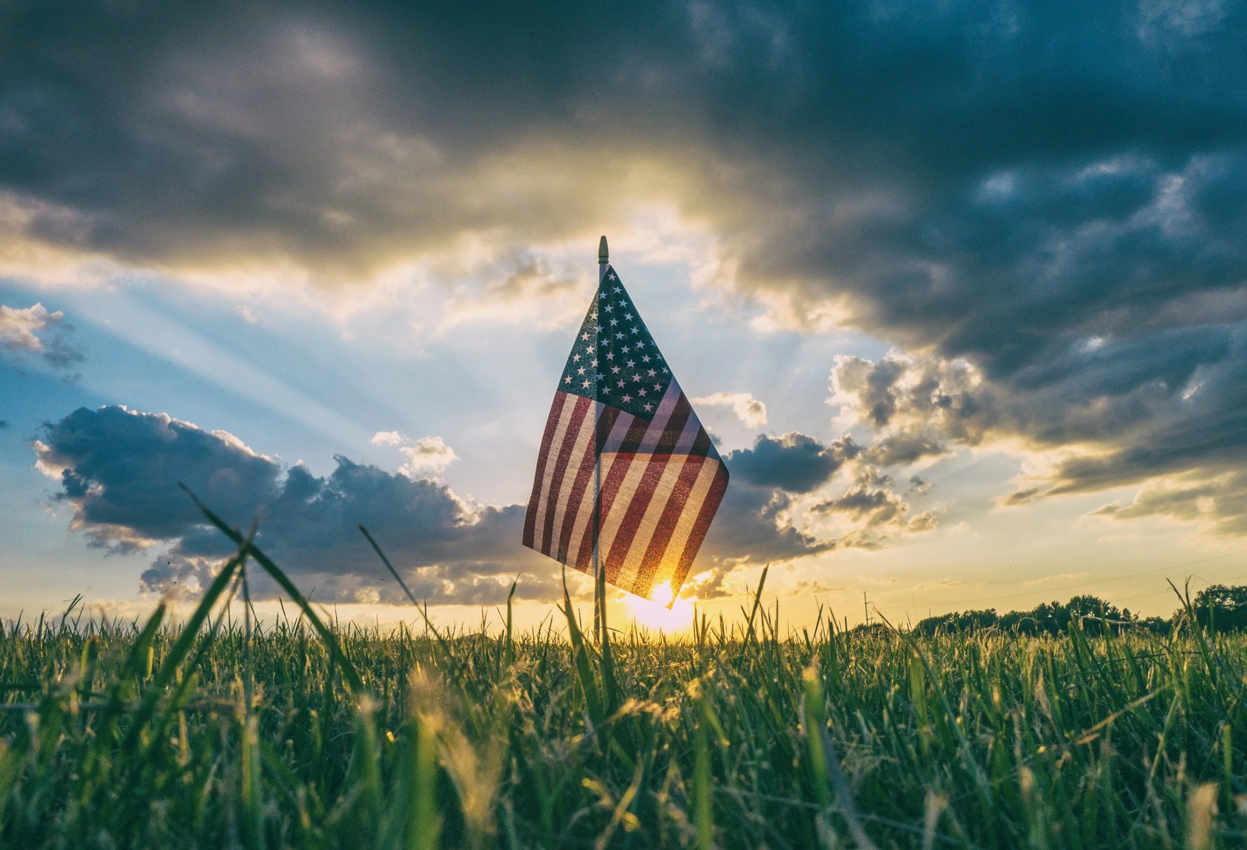 American flag waving in a field at sunset with clouds in the sky.