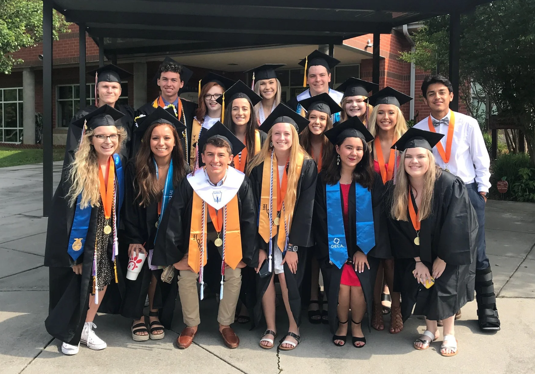 Group of diverse high school graduates in caps and gowns posing for photo outdoors