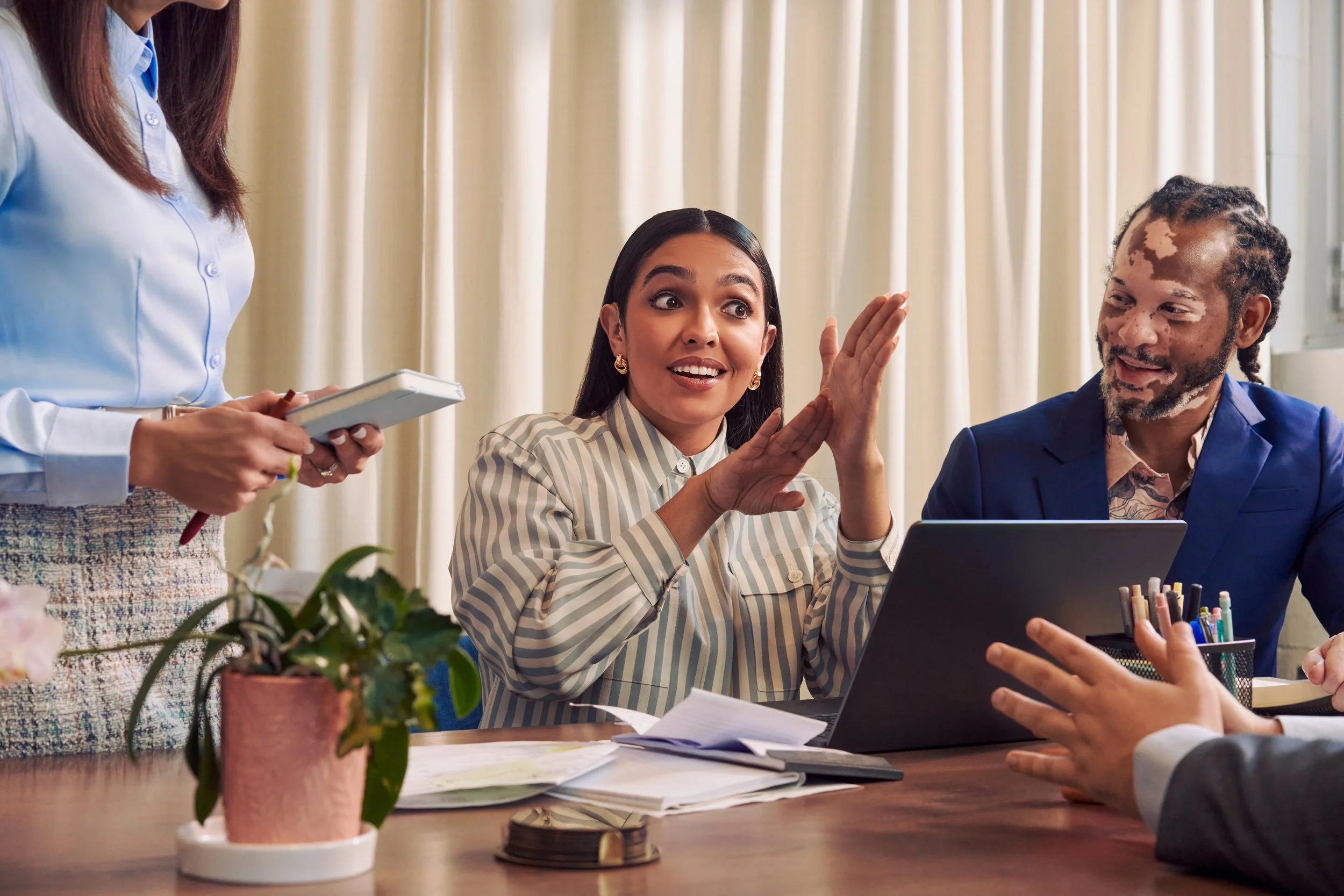 A Deaf Latina woman communicates in American Sign Language to colleagues in a conference room meeting.
