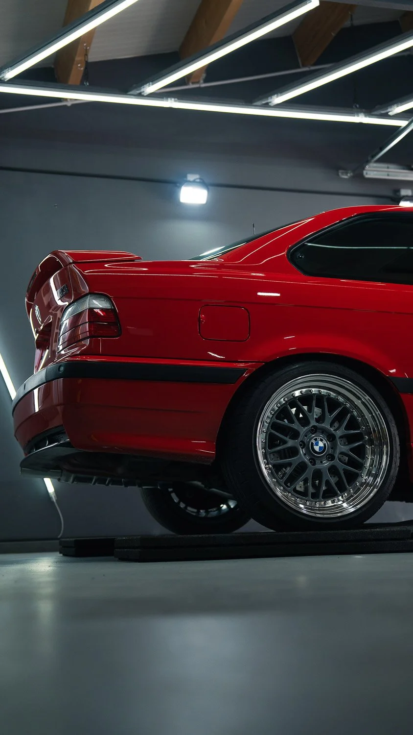 Ein roter BMW-Sportwagen in einer modernen Garage mit Beleuchtung und Holzdecke.