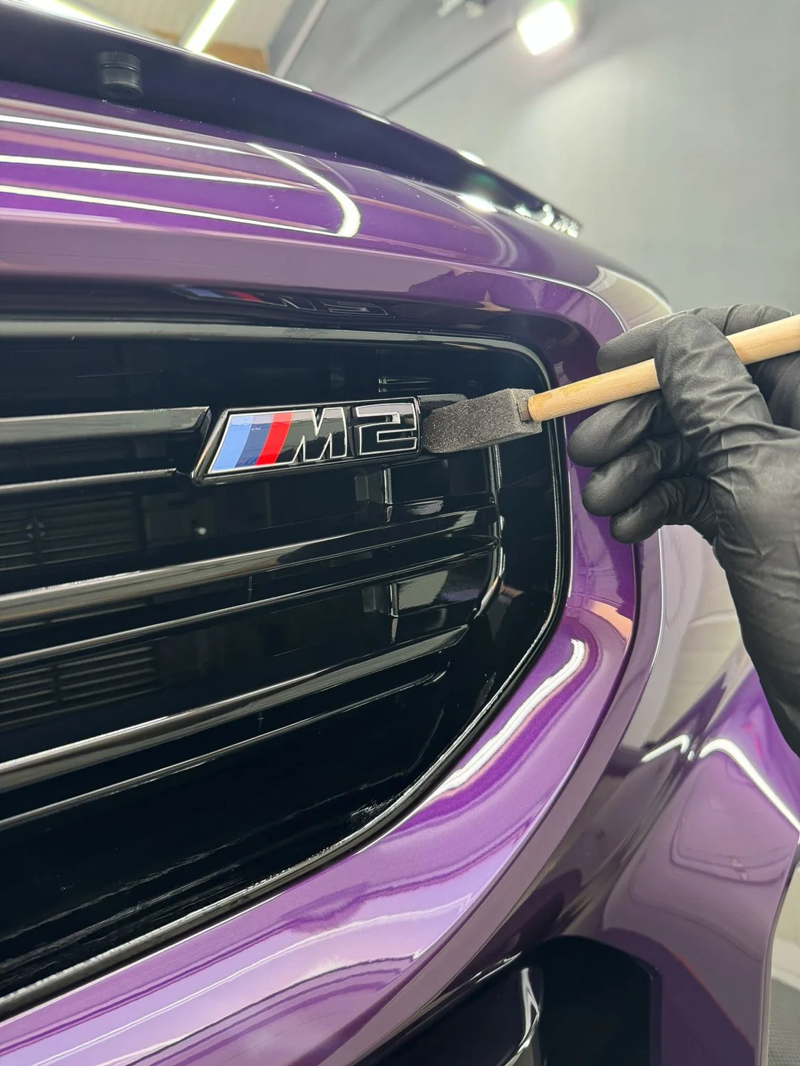 Hand, die mit einem Pinsel das M2-Emblem an einem schwarzen und lila BMW fasst.