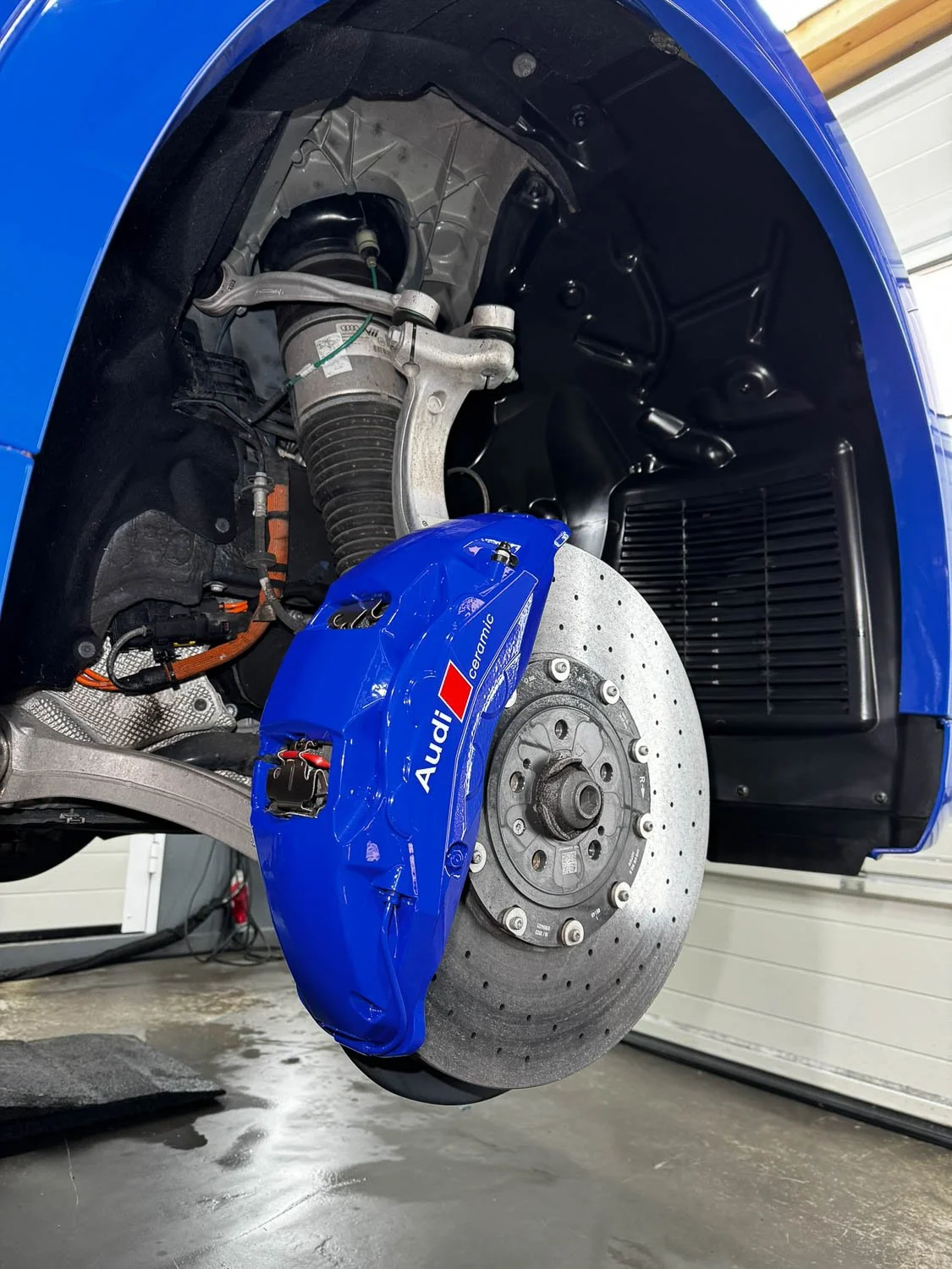 Bremsscheibe und Bremssattel eines blauen Audi Rennwagens, der in einer Werkstatt ohne Reifen steht.