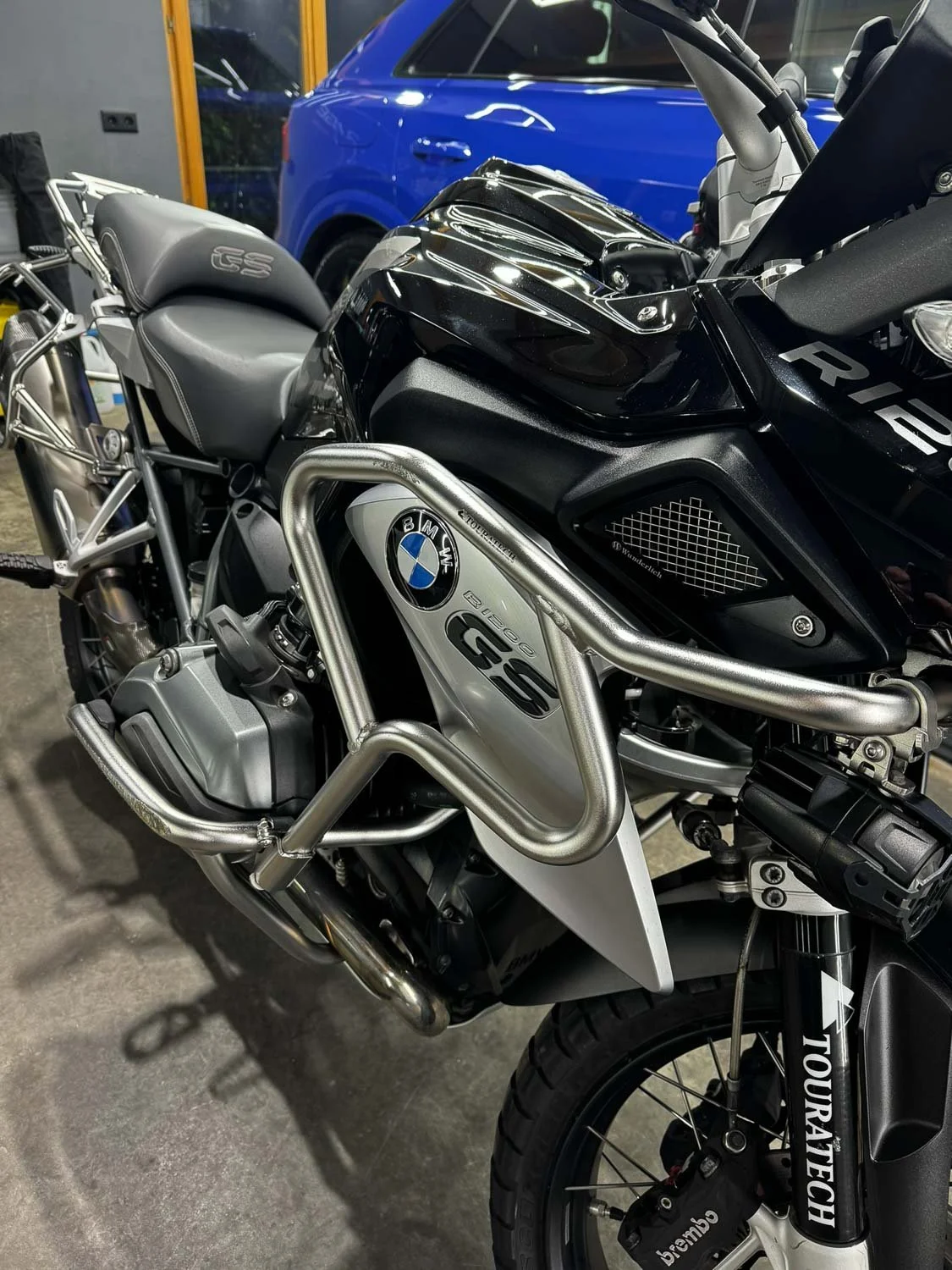 Schwarzer BMW GS Motorrad Enduro-Motorrad im Kofferraum einer Garage, im Hintergrund ein blauer Wagen.