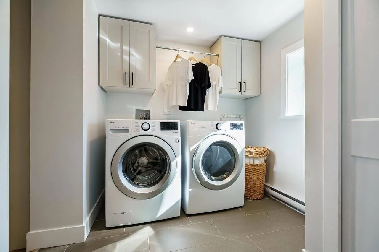 Laundry room with a front-loading washer and dryer, hanging clothes, cabinets, a laundry basket, and a window