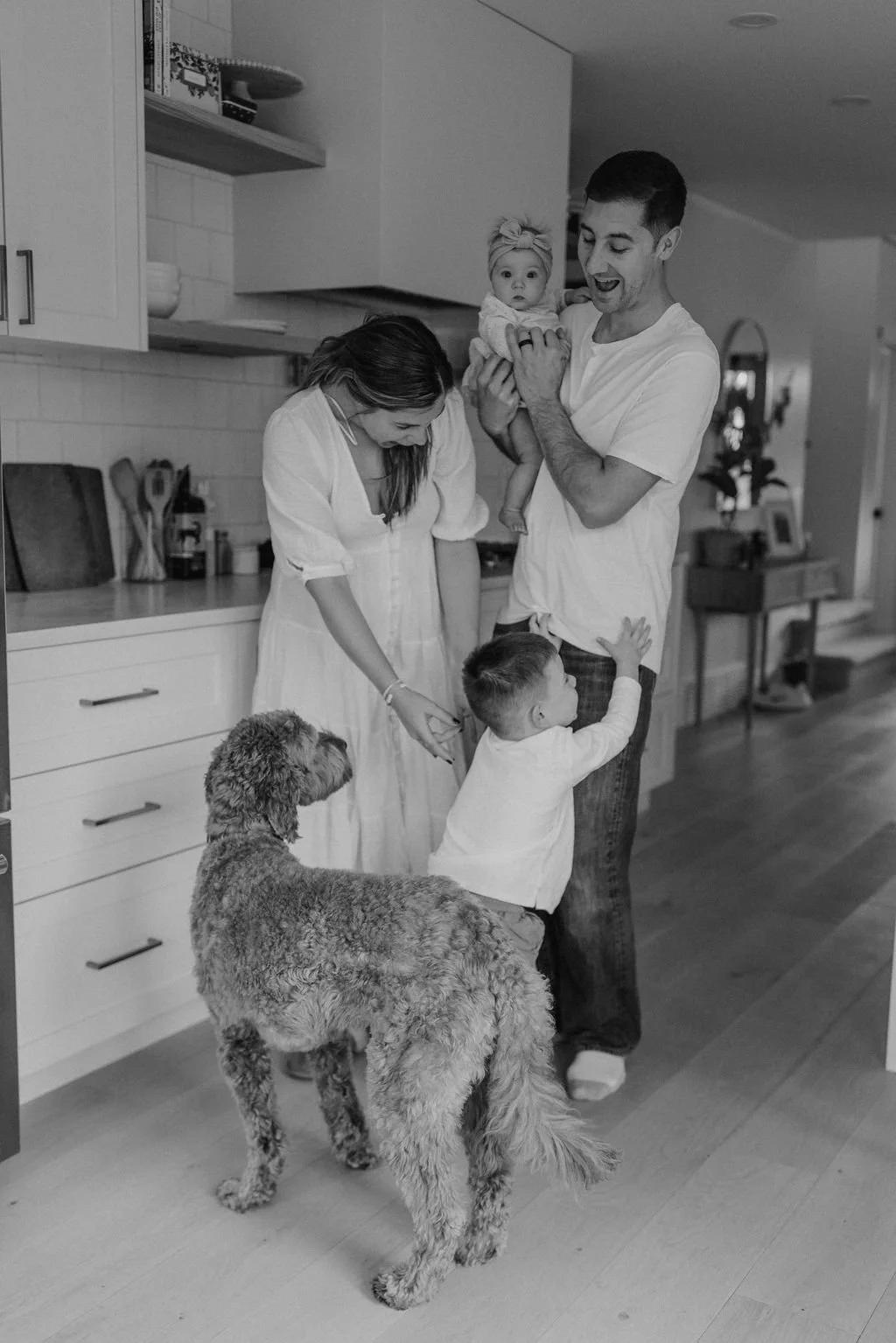 Family in the kitchen with two children, a woman, a man holding a baby, and a dog.