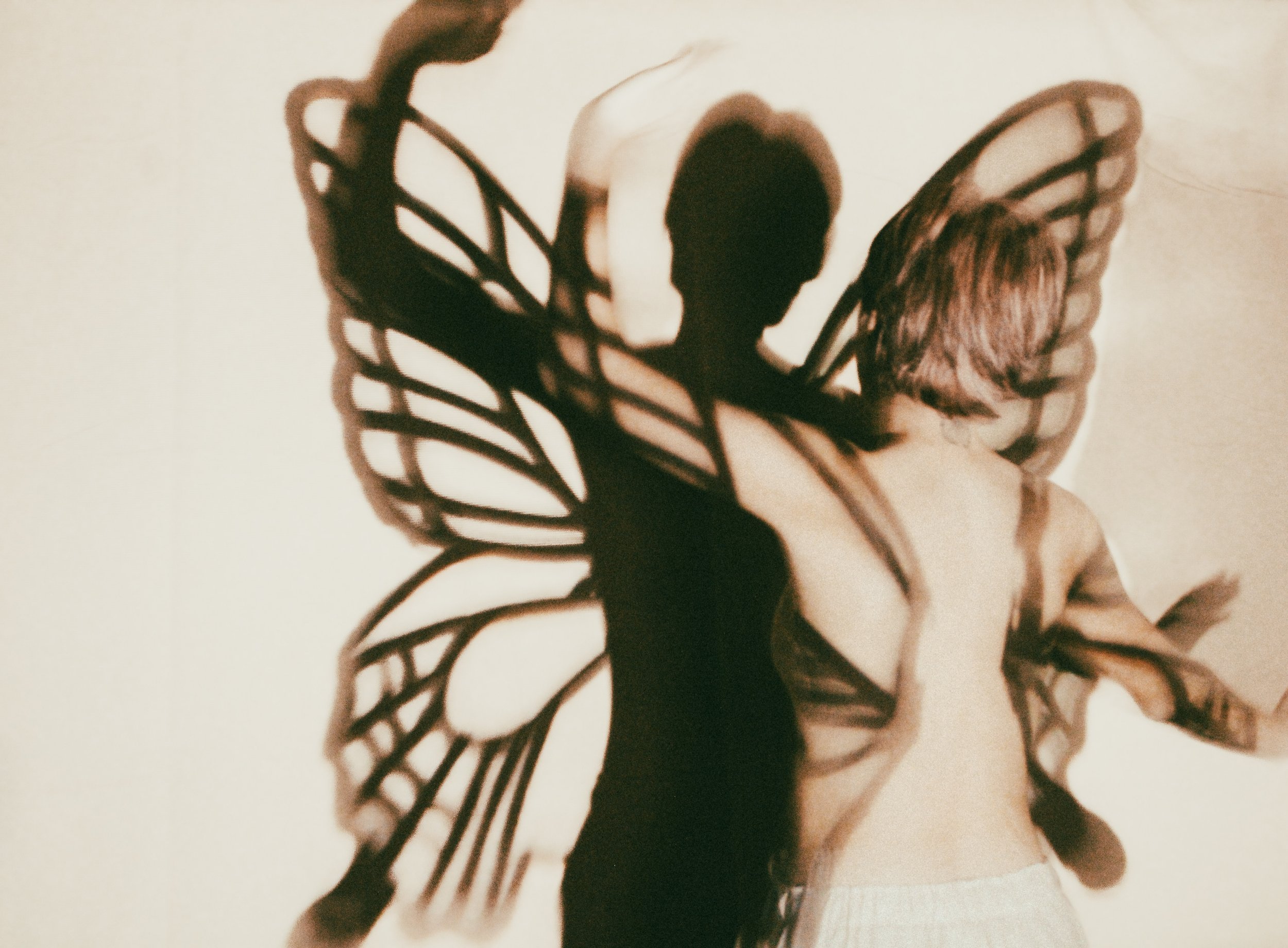 The shadow of a shirtless child with butterfly wings cast on a wall, resembling a fairy or butterfly figure.