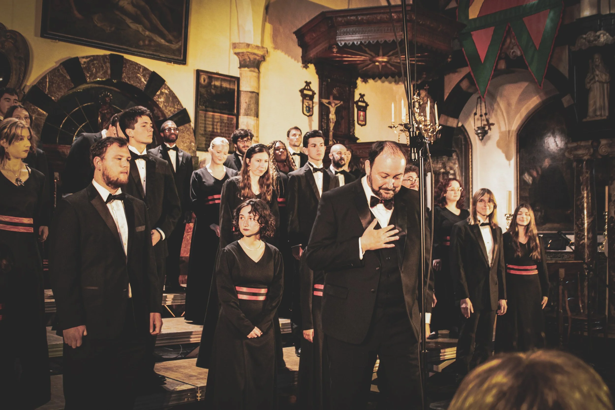 A choir dressed in black with red accents performing in a historic church with ornate decorations and religious symbols.