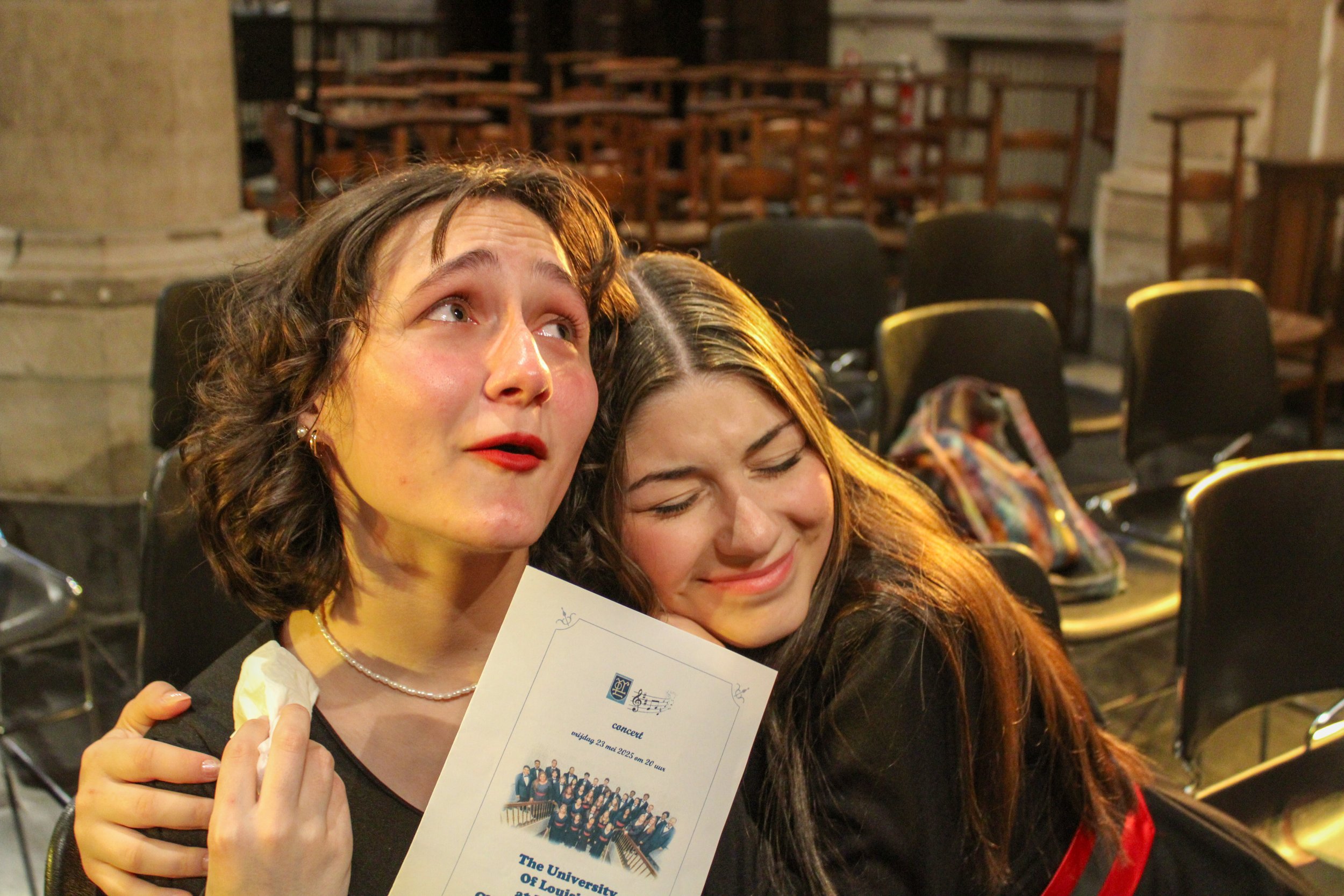 Two women hugging in a concert hall, one holding a program for 'The University of Missouri' concert.