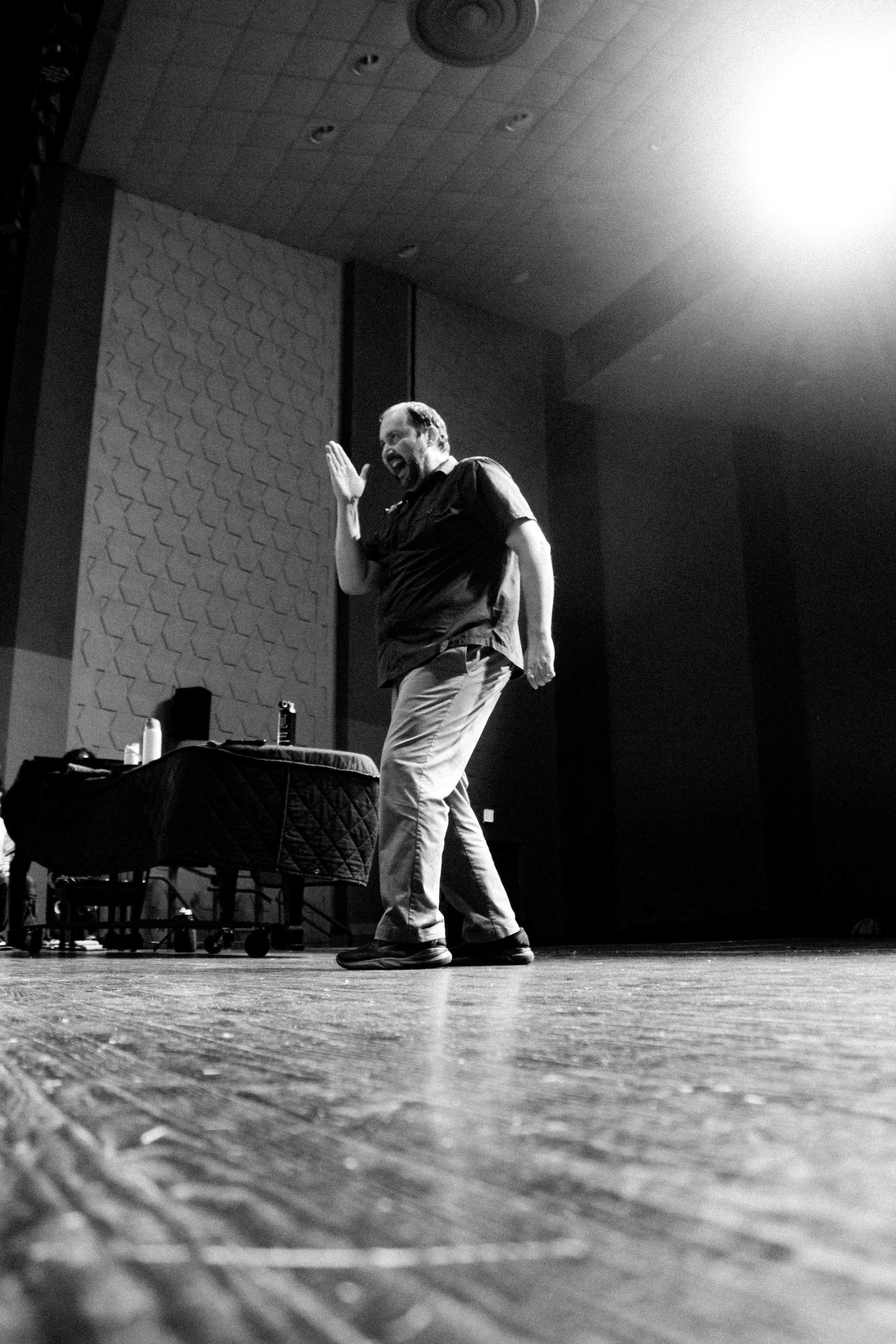 A man on stage laughing and gesturing with his hand during a performance or lecture.