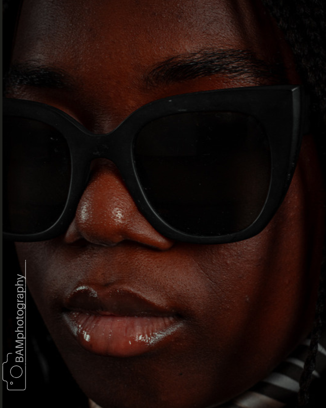 Close-up of a person wearing black sunglasses and a striped shirt. The person's face is partially visible, highlighting the nose, lips, and sunglasses.