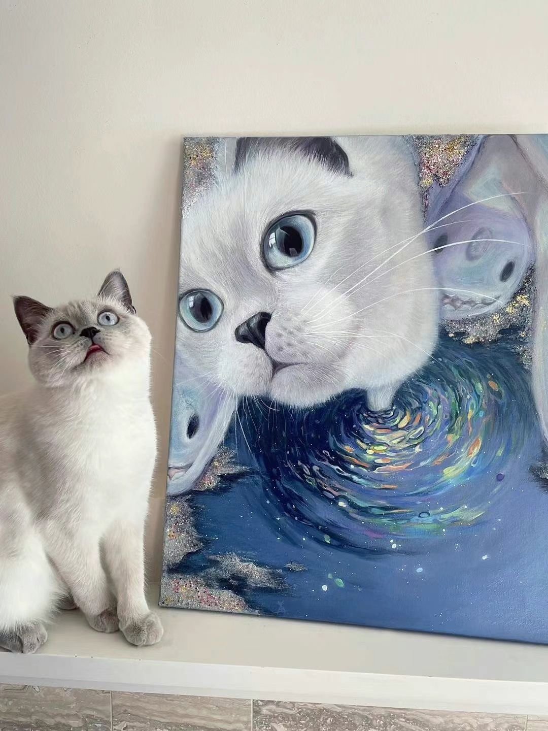A realistic painting of a white kitten with blue eyes, with another cat and a swirling water pattern around its head, displayed on a wall.