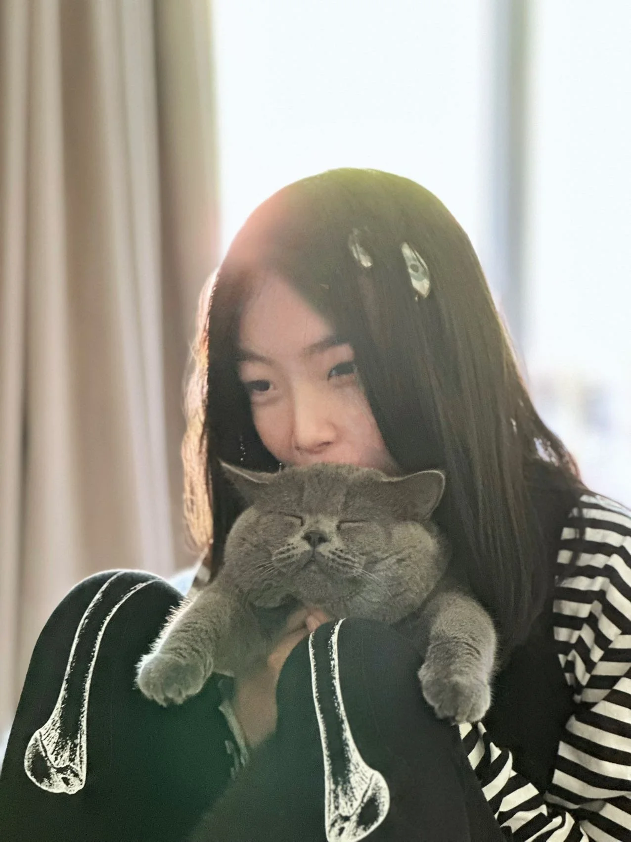 A woman with long dark hair holding a gray cat with closed eyes, both appearing content.