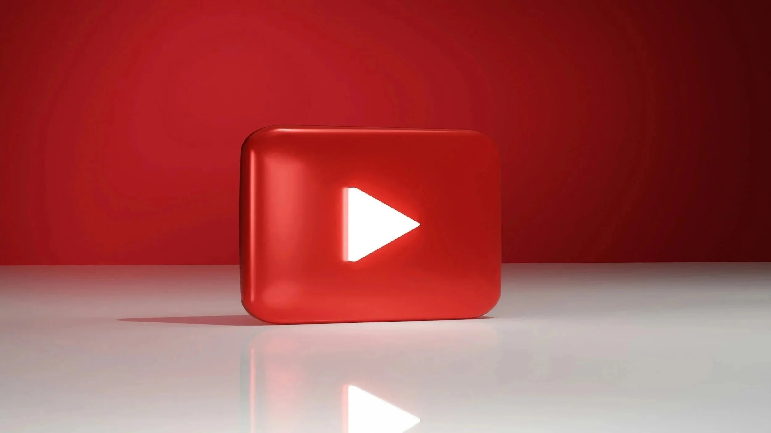 A red, rounded rectangular YouTube play button icon on a white surface with a red background.
