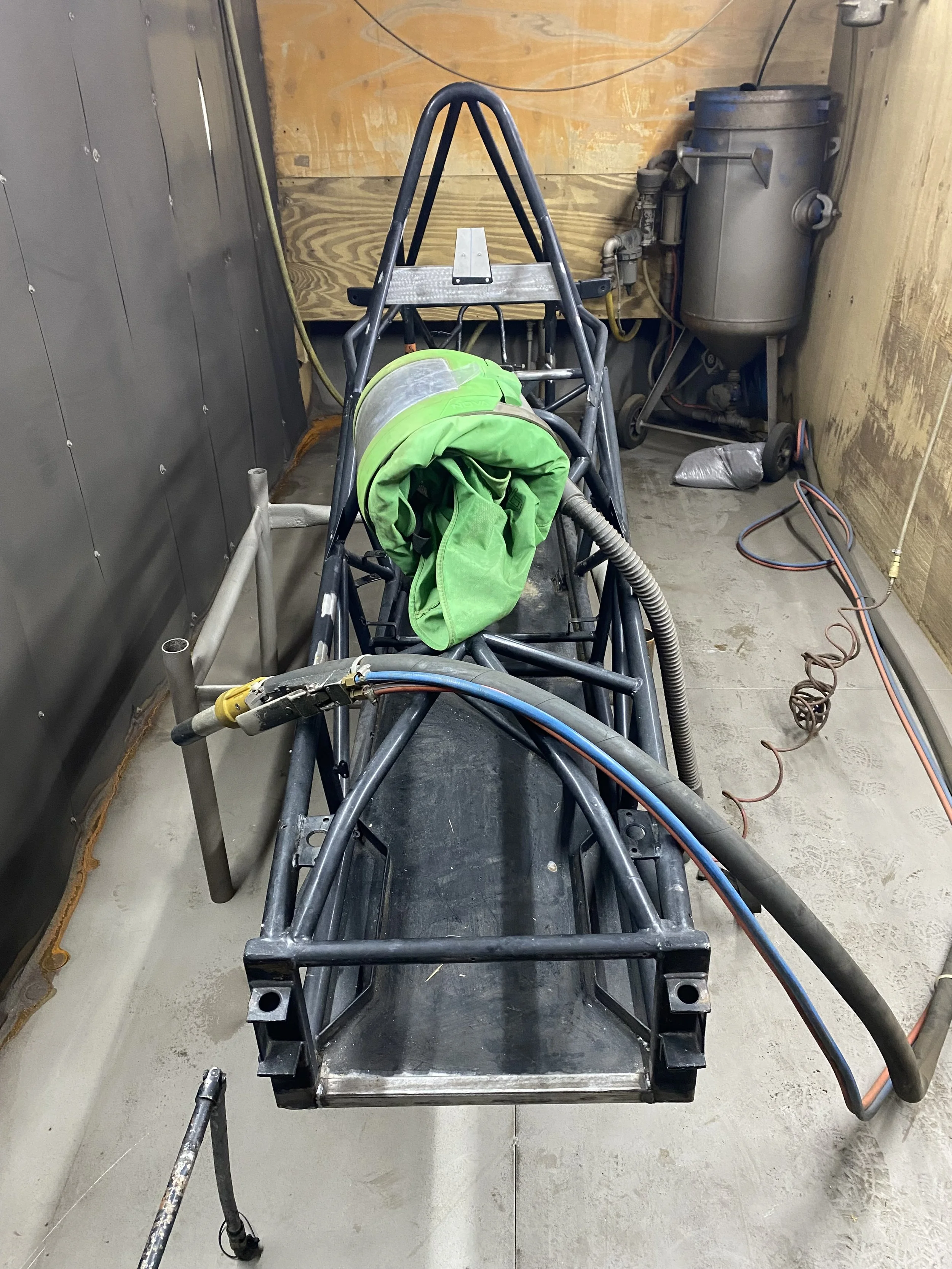 A partially assembled black metal frame with a green fabric cover inside a room under construction, with tools, wires, and construction materials visible.