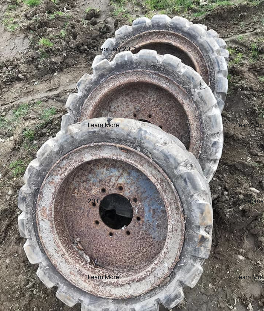 Three rusty large tractor tires stacked on soil outdoors.