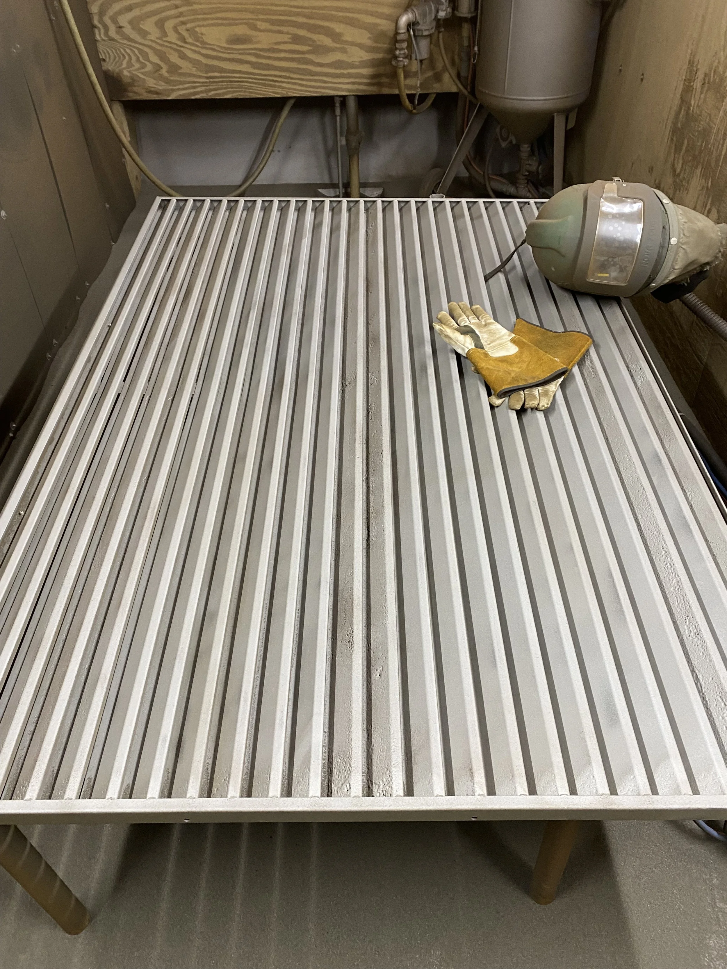 A metal work table with a pair of protective gloves on it, located in a workshop or industrial setting.