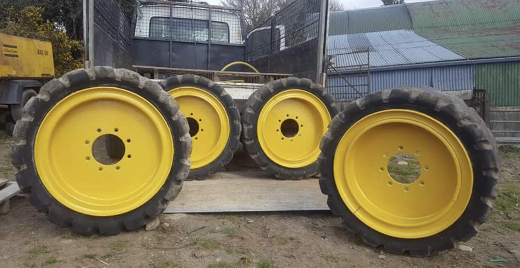 Four large yellow tractor wheels with black tires stacked and placed on the ground.