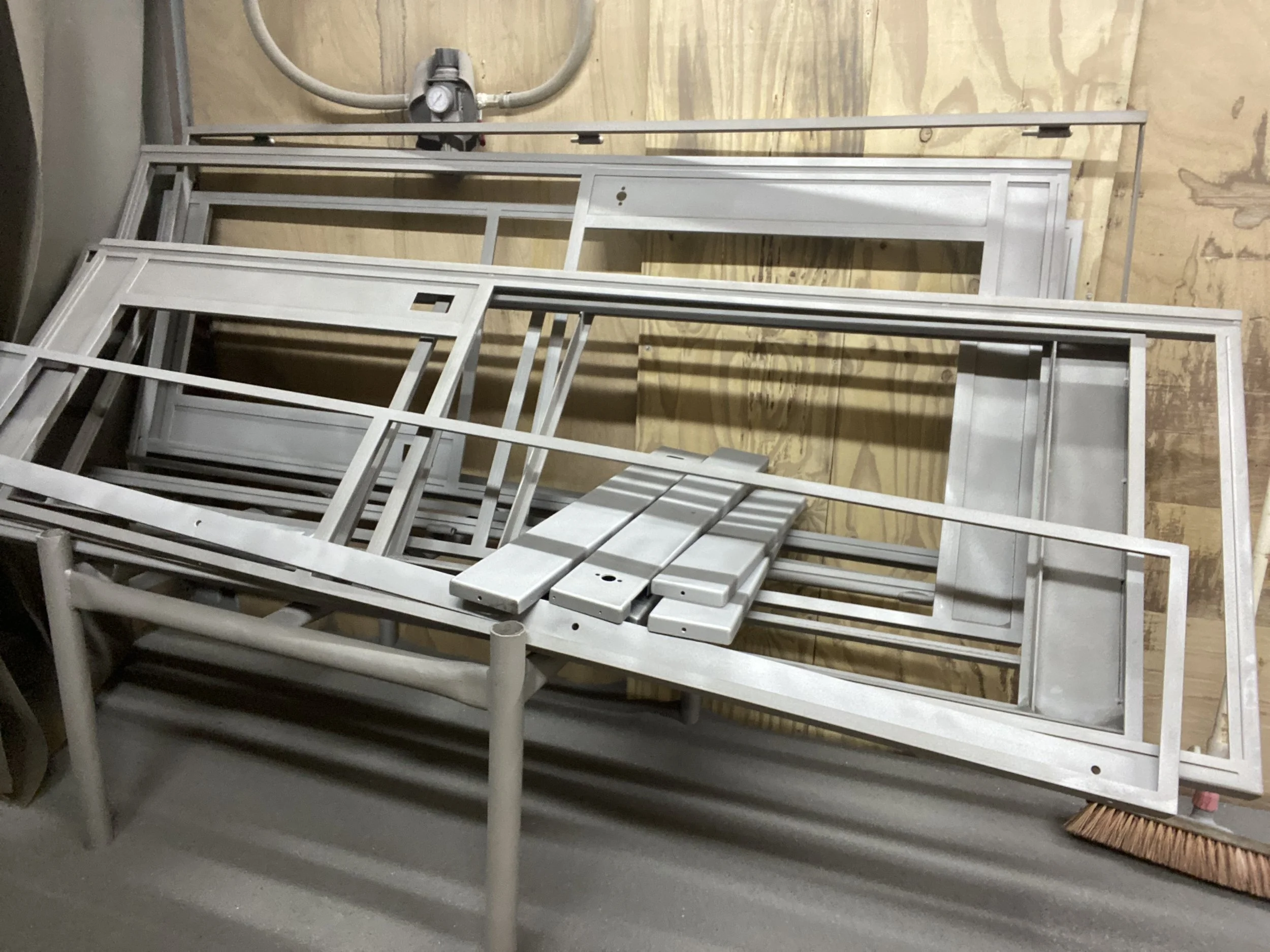 Metal window frames and parts stacked on a wooden surface in a workshop.