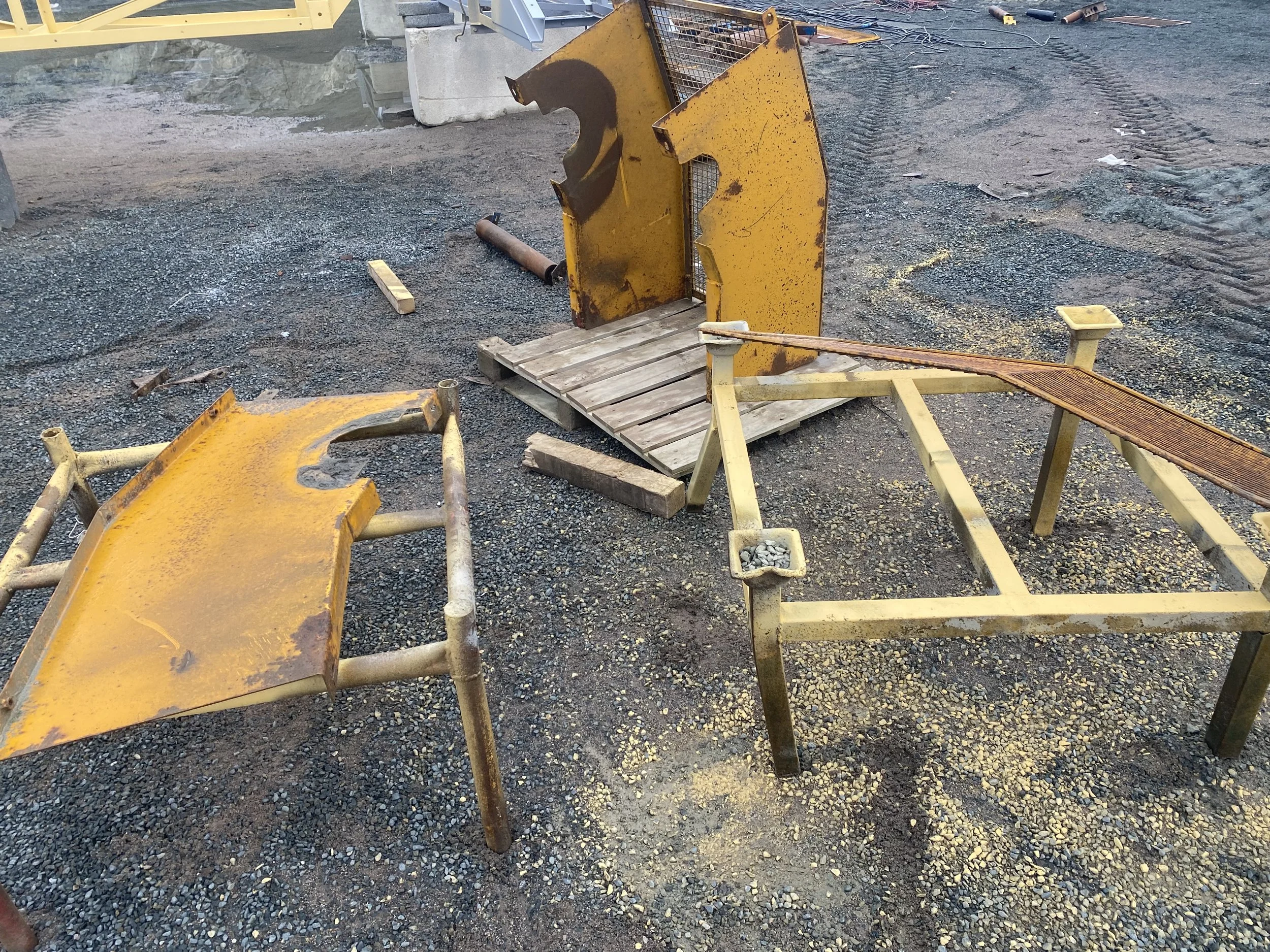 Construction site with broken yellow metal frames, a wooden pallet, and loose gravel on the ground.