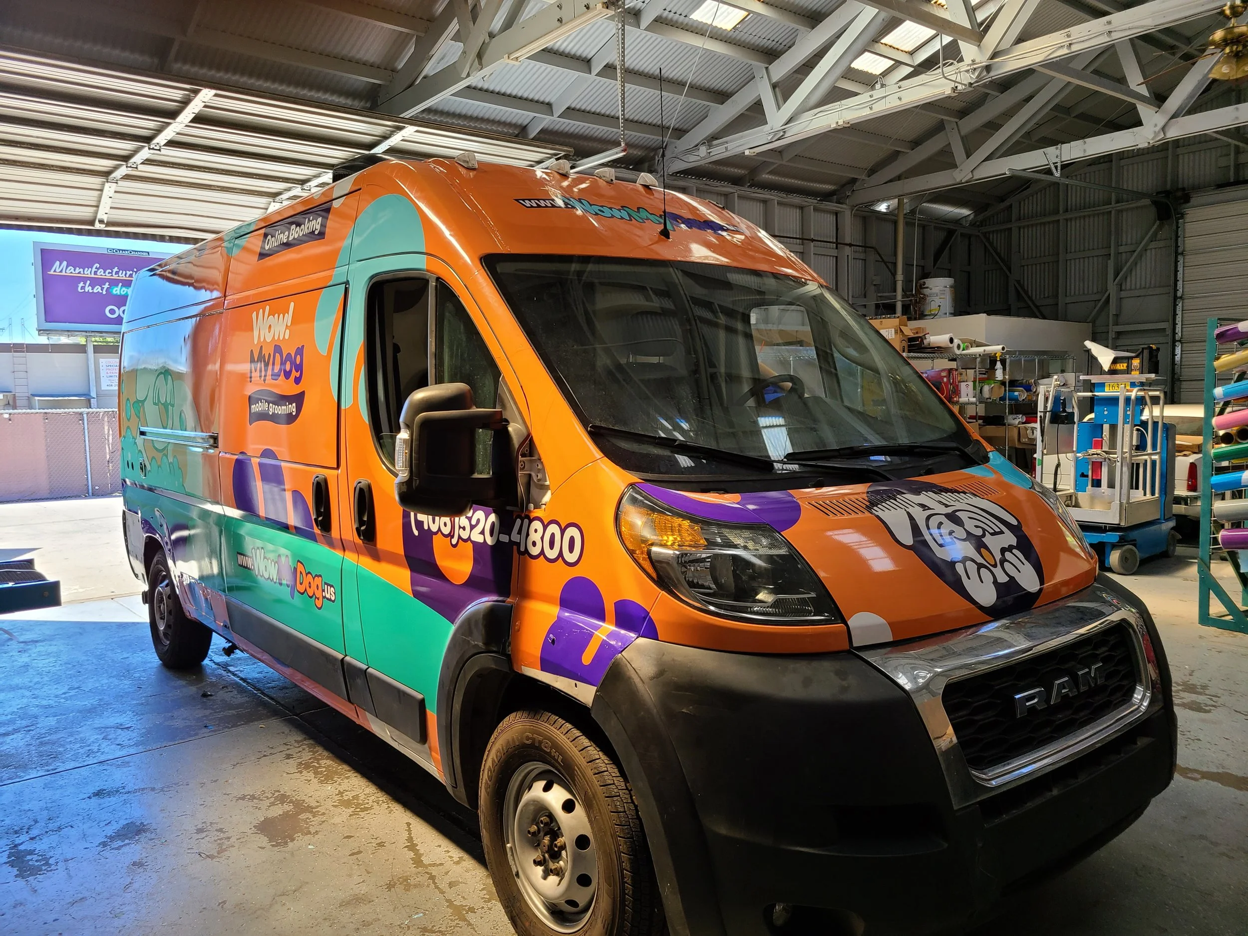 A colorful branded van inside a warehouse with signage for 'Wow! MyDog' mobile grooming and adoption services, surrounded by various equipment and supplies.