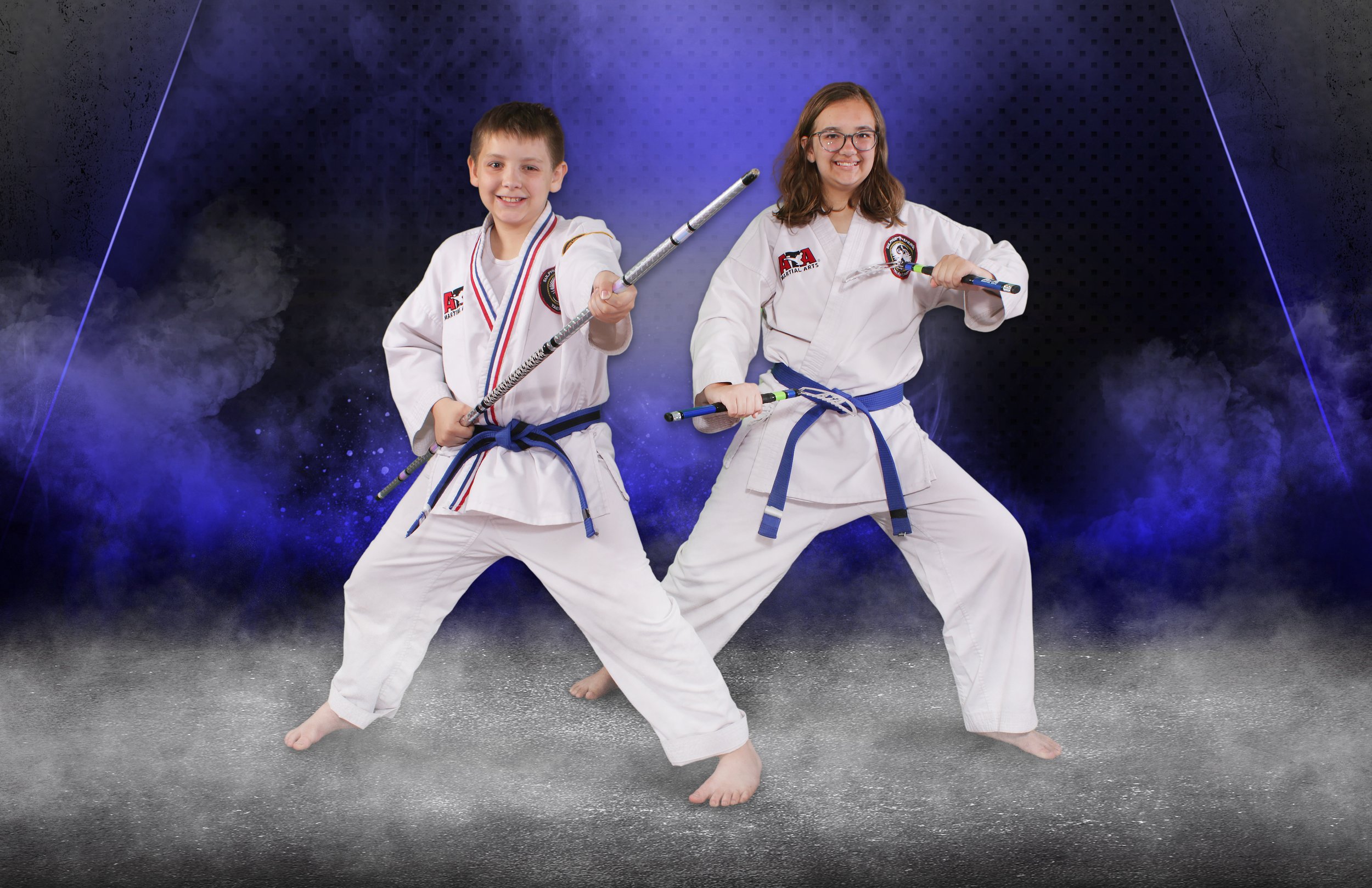 Two children practicing martial arts in taekwondo uniforms with blue belts, using weapons, against a digital space-themed background.