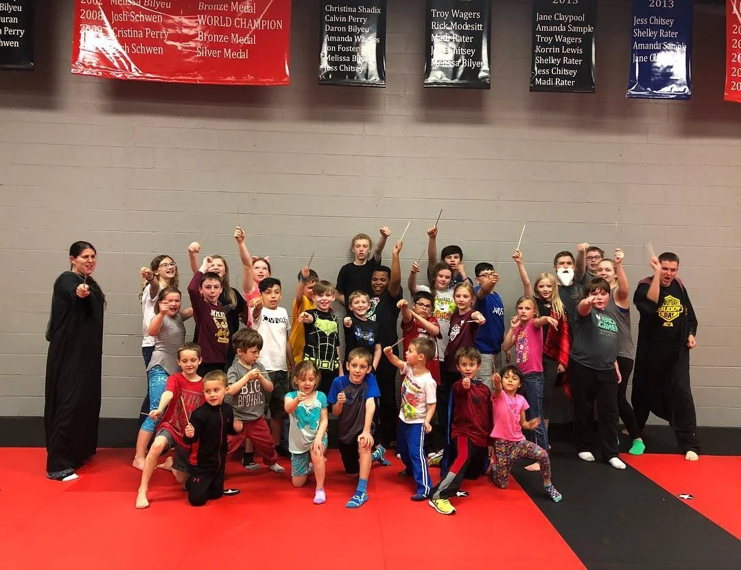 A group of children and an instructor in a martial arts dojo, posing with fists raised after class.