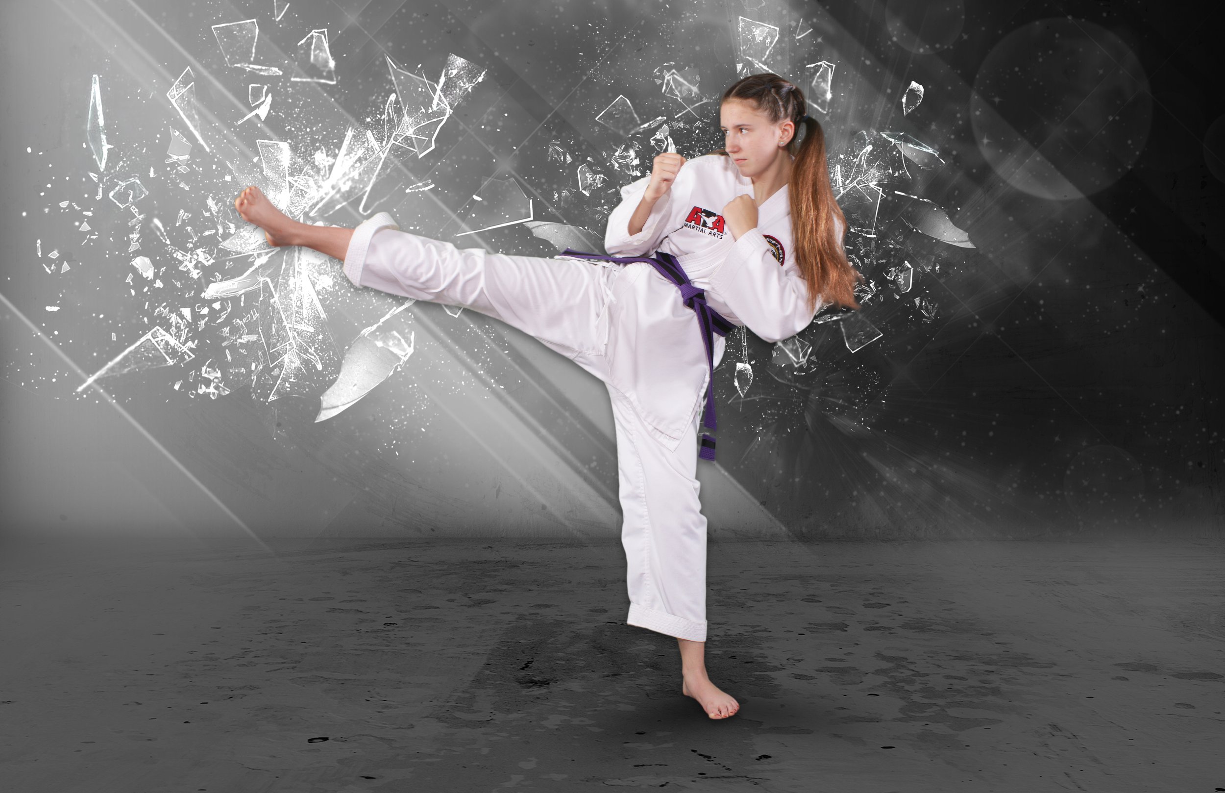 Young girl practicing taekwondo in a white martial arts uniform with a purple belt, performing a high kick against a digital shattered glass background.
