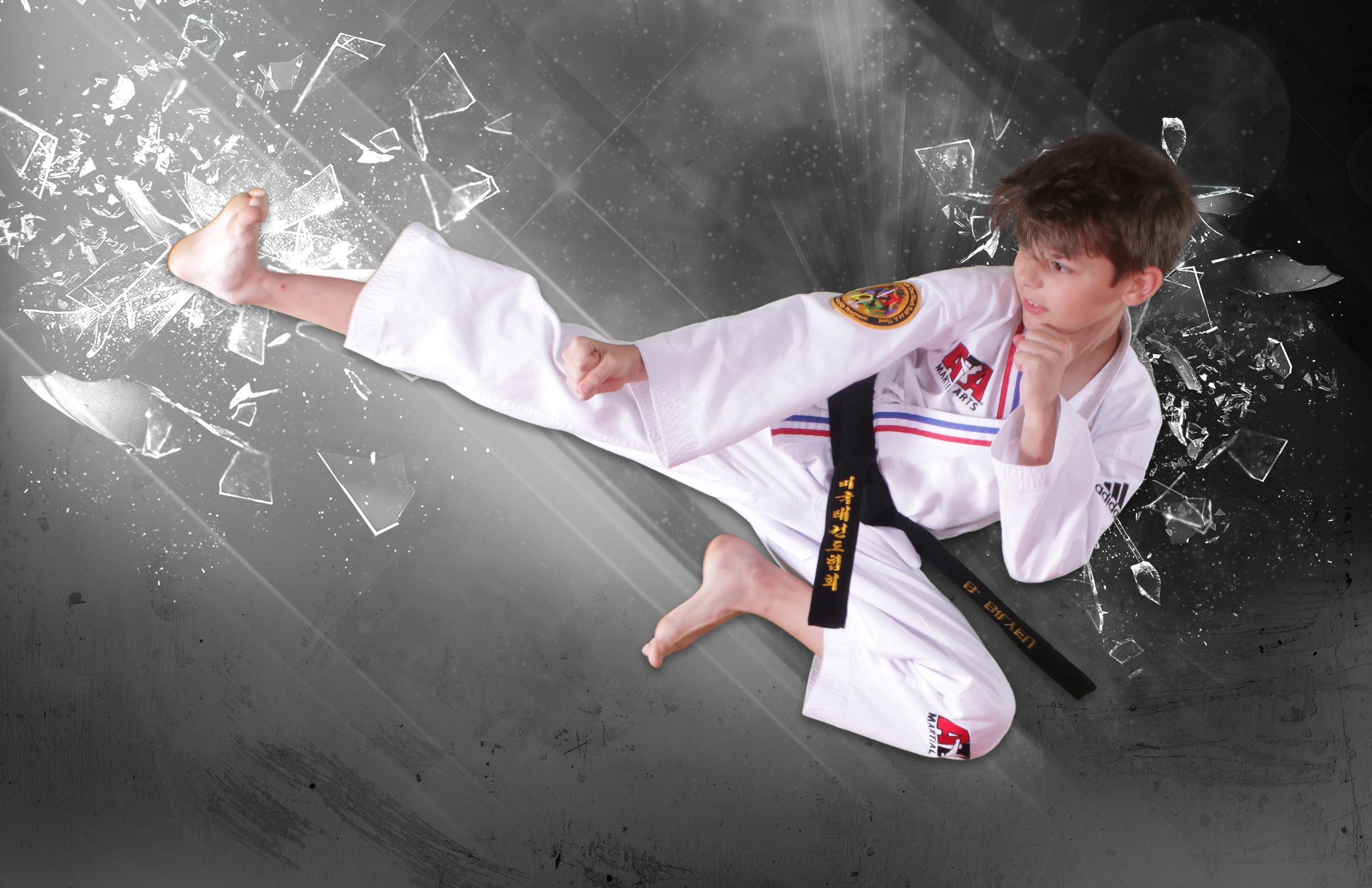 Young boy in a martial arts uniform performing a side kick, with a background of broken glass effects.