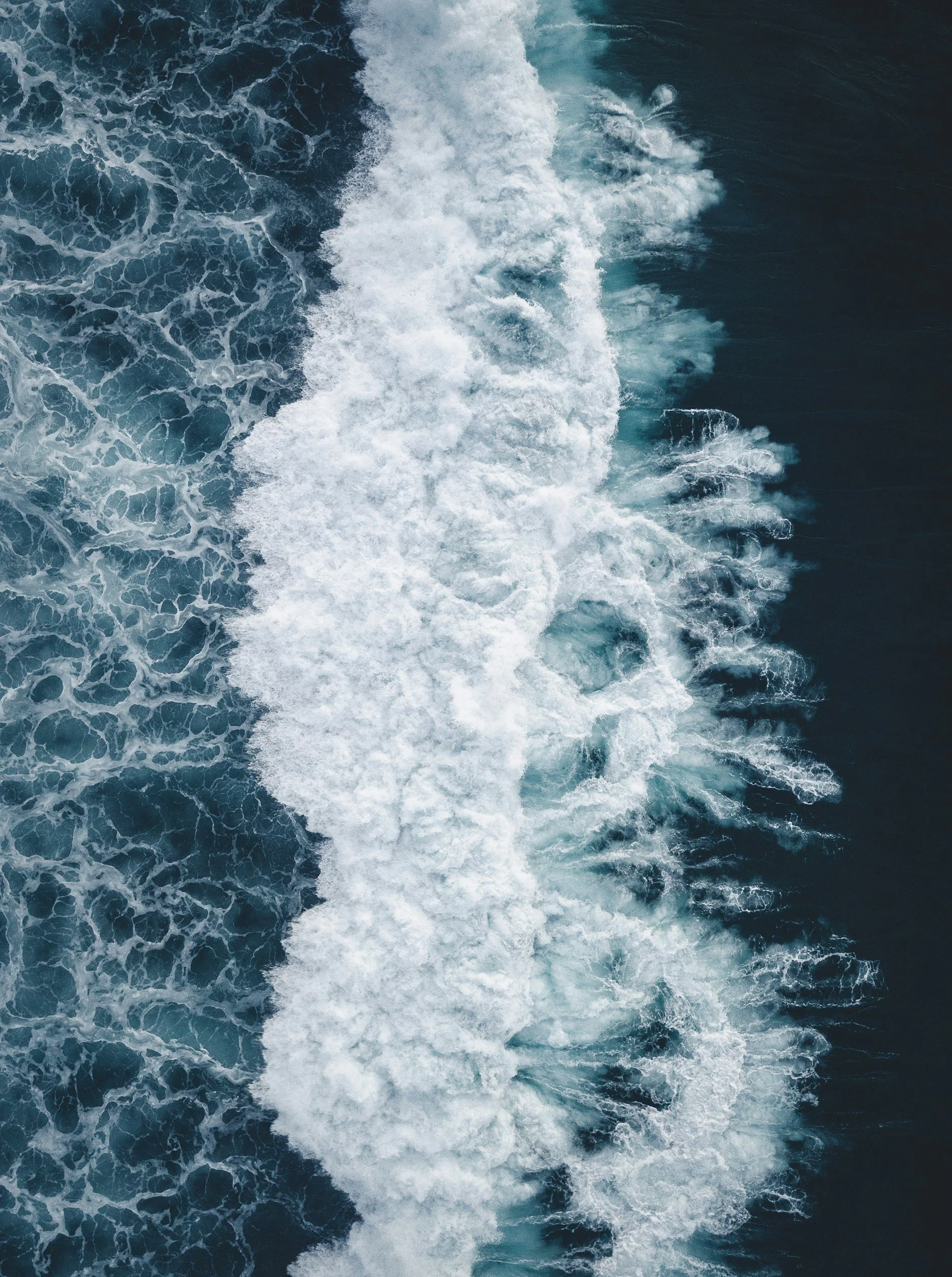Aerial view of ocean waves with white foam and dark blue water.