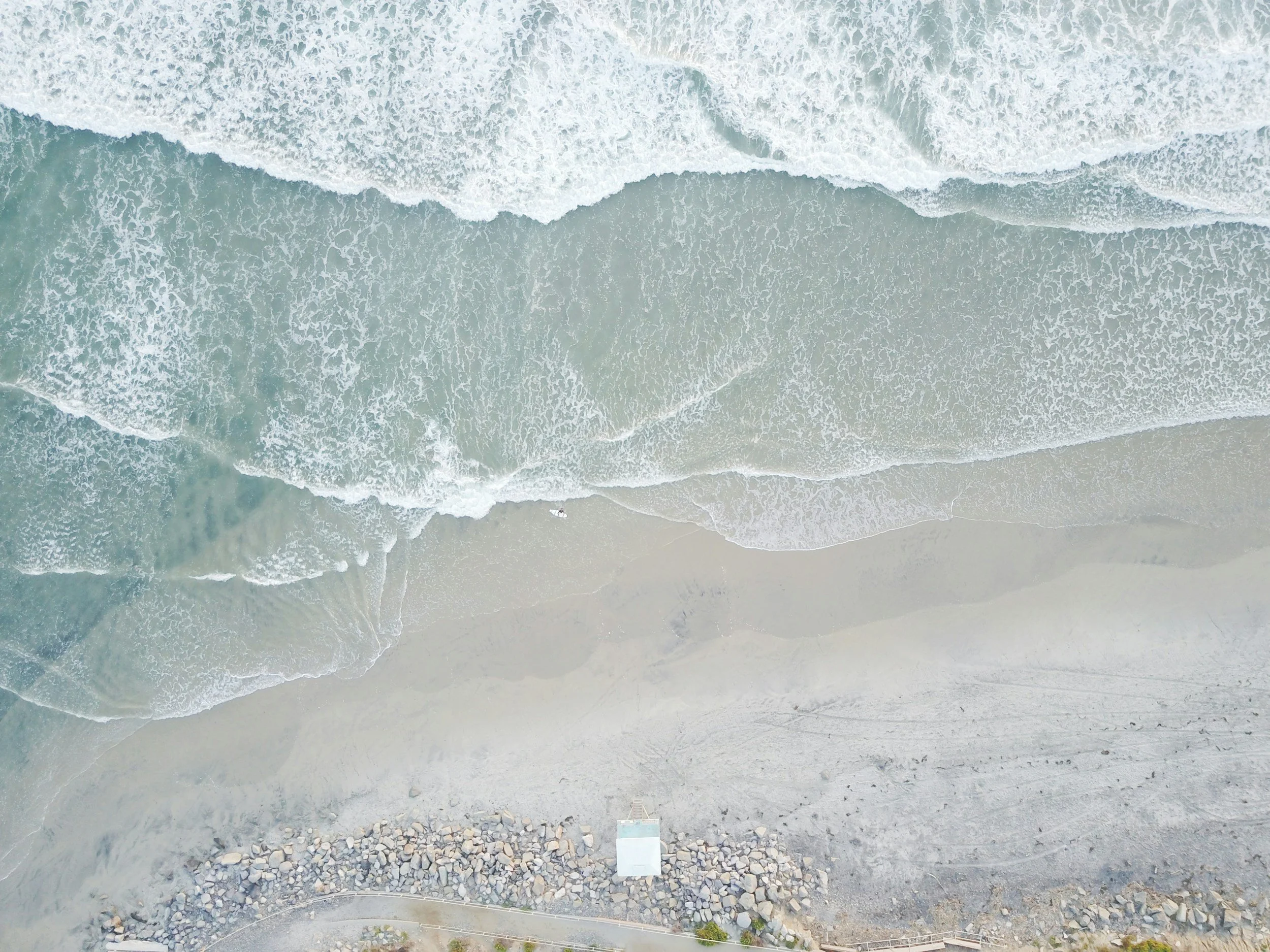 An aerial view of a sandy and rocky beach with waves crashing onto the shore.