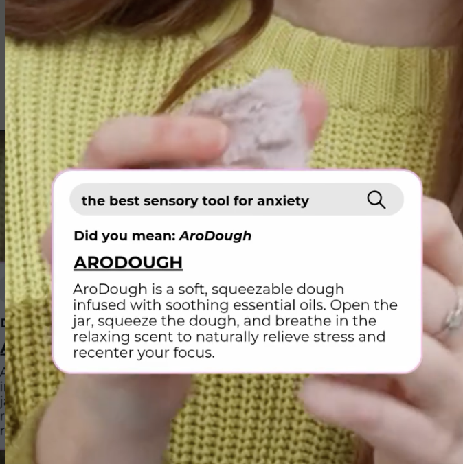 Person wearing a yellow sweater holding a small soft, squeezable jar of AroDough dough infused with essential oils, with an informational label about its benefits for stress relief.
