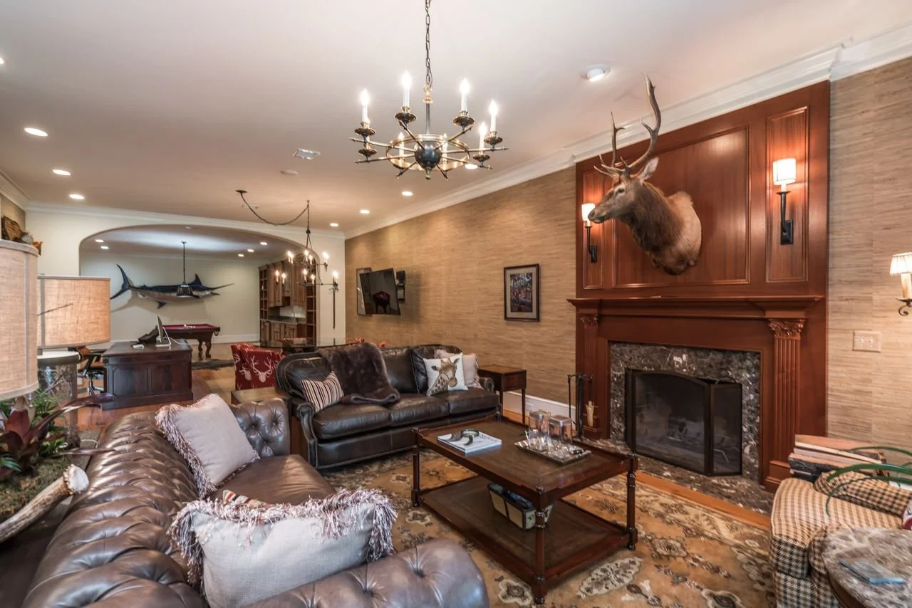 Living room with deer head mounted above fireplace, leather sofas, wall-mounted TV, and various decorative items.