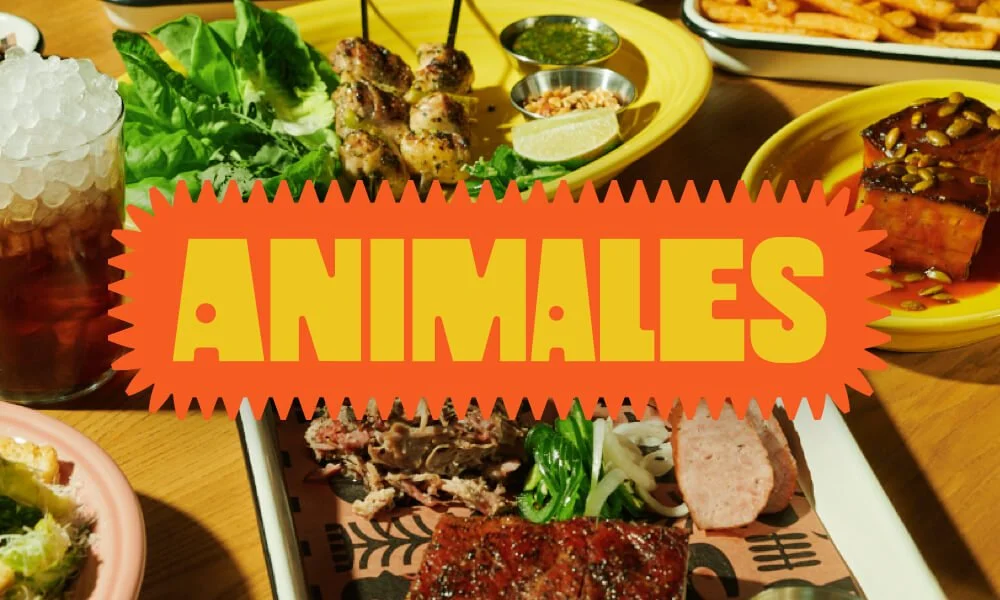 A photo of a tabletop spread of various barbecued meats, side dishes, and drinks, with the "Animales" logo superimposed