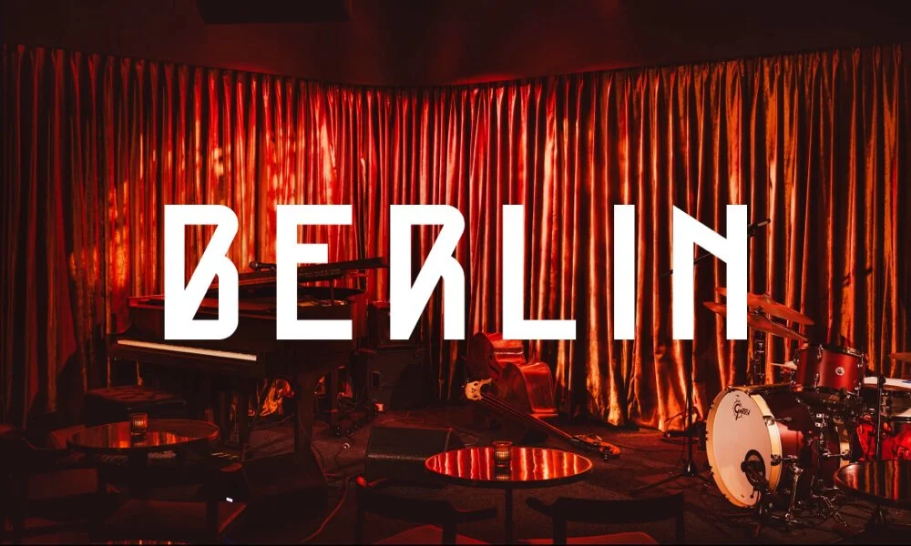 A photo of a music lounge stage with a dark, heavily red ambiance, with a logo that says "Berlin" superimposed
