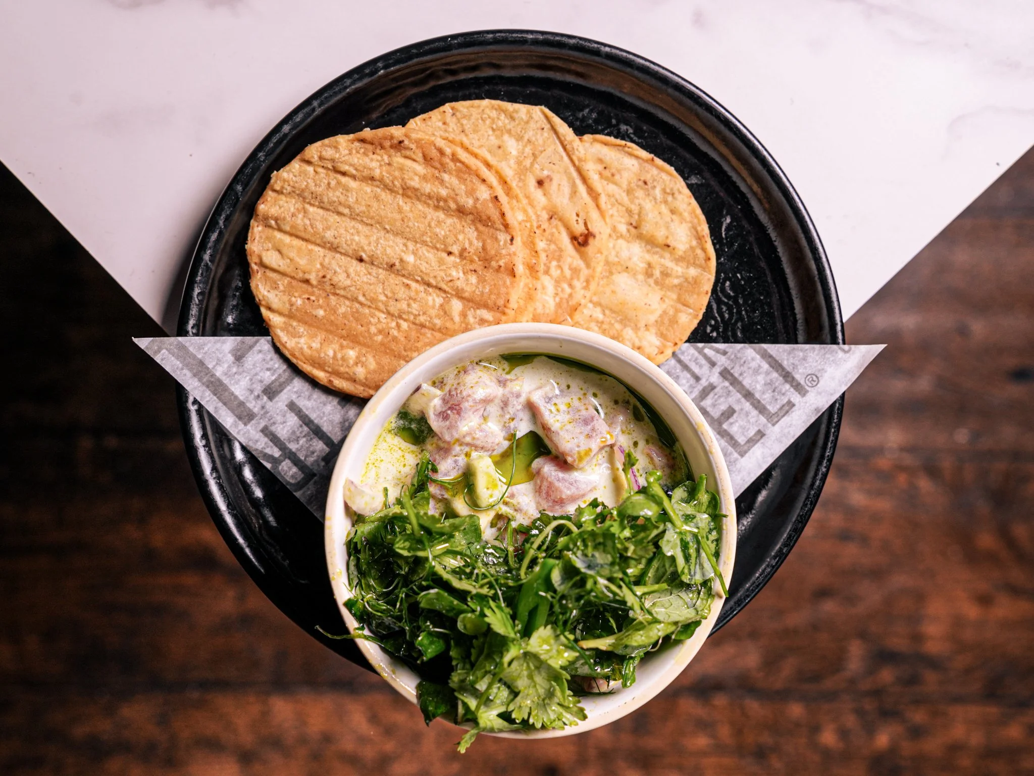 Top view of a black plate with three crispy, golden-brown tortilla chips and a small white bowl of green cilantro and onion salsa.