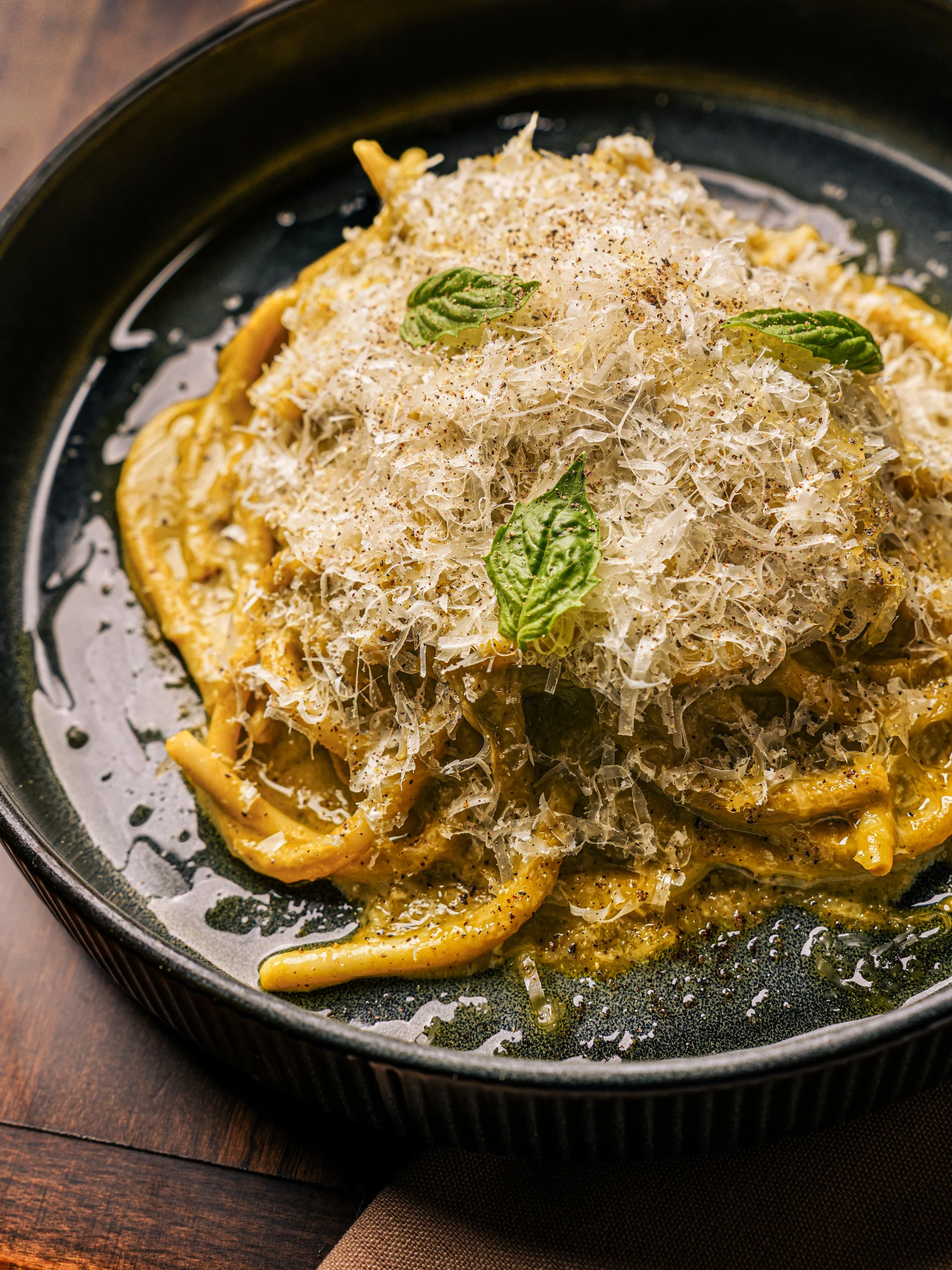 Creamy pasta dish topped with grated cheese and fresh basil leaves, served on a black plate.
