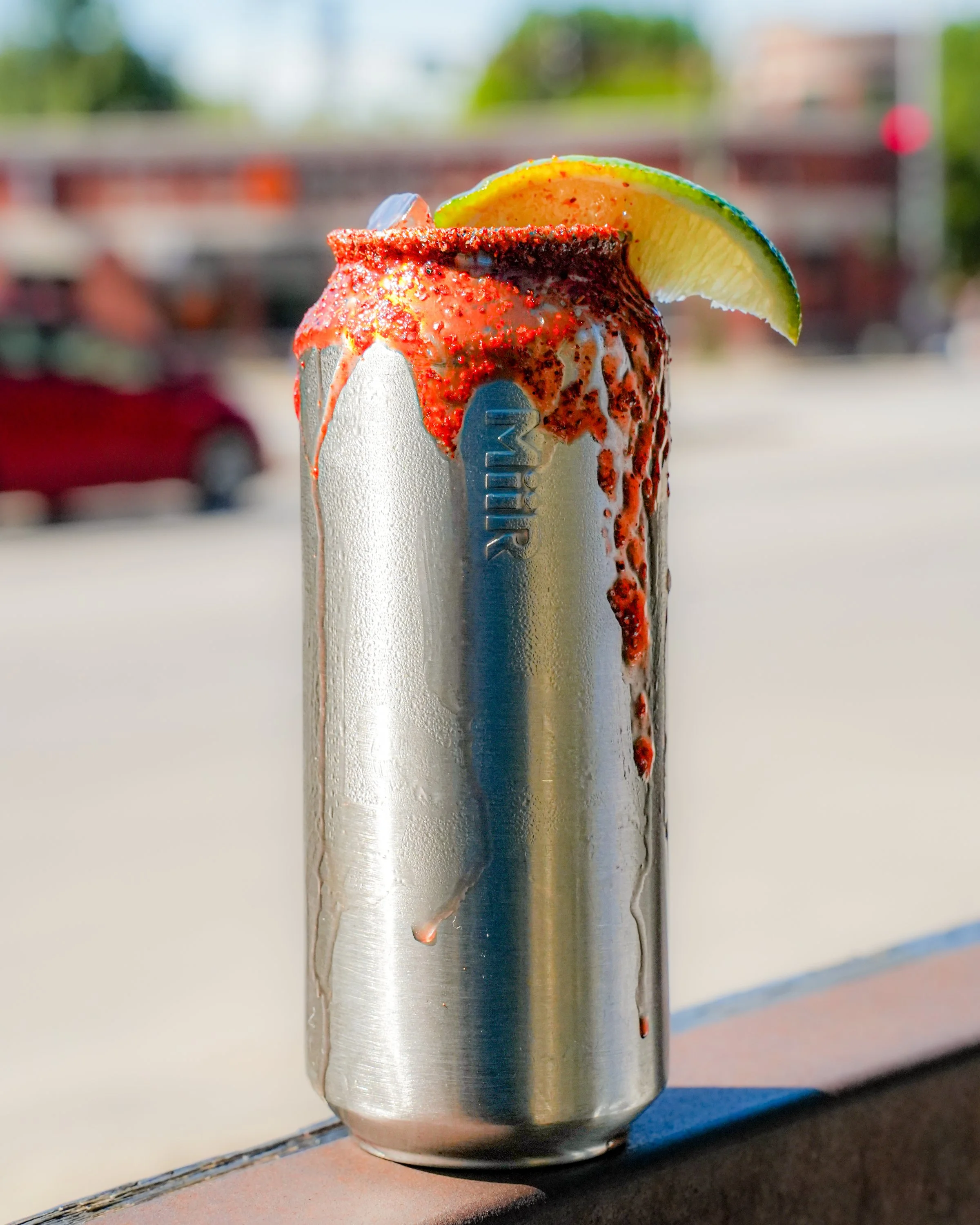 Close-up of a stainless steel vape pen with red flavored e-liquid dripping from the mouthpiece, garnished with a lime wedge.