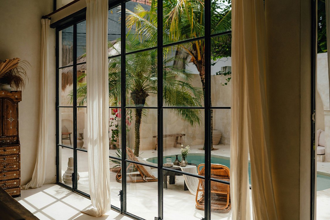 Very large steel window with grilles looking out at a pool in the bedroom of a large Tuscan-style home.