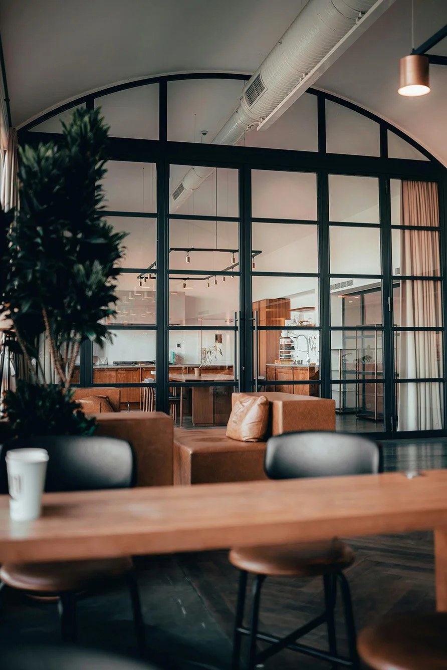 Very large arching, steel and glass divider with grilles in a commercial space. Divider contains two steel and glass French doors with grilles.