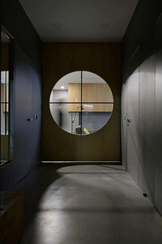 Large round windows with grilles inside a dark painted hallway looking onto a second room.