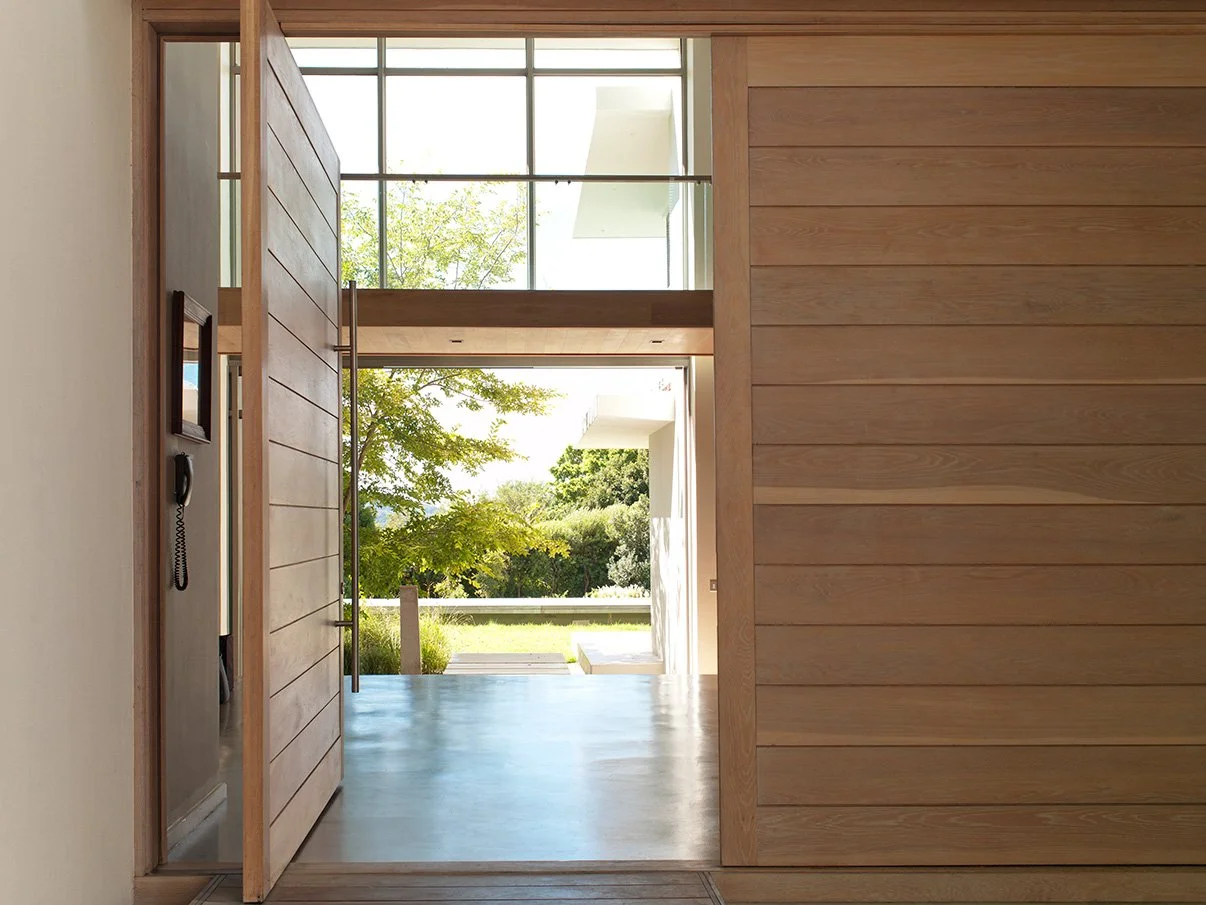 Very large wood pivot entry door of a luxury home that is open and looking at the outside.