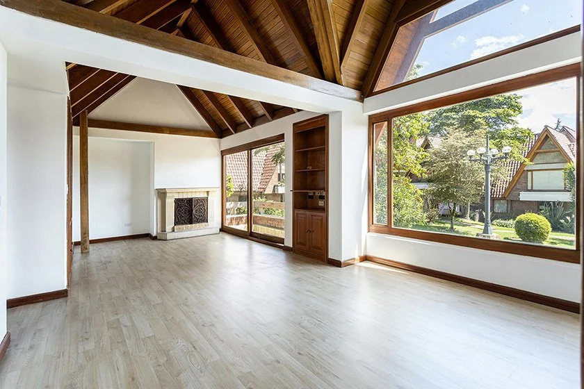 Large empty room with an expansive wood-framed picture window and sliding door looking out at an affluent neighborhood.