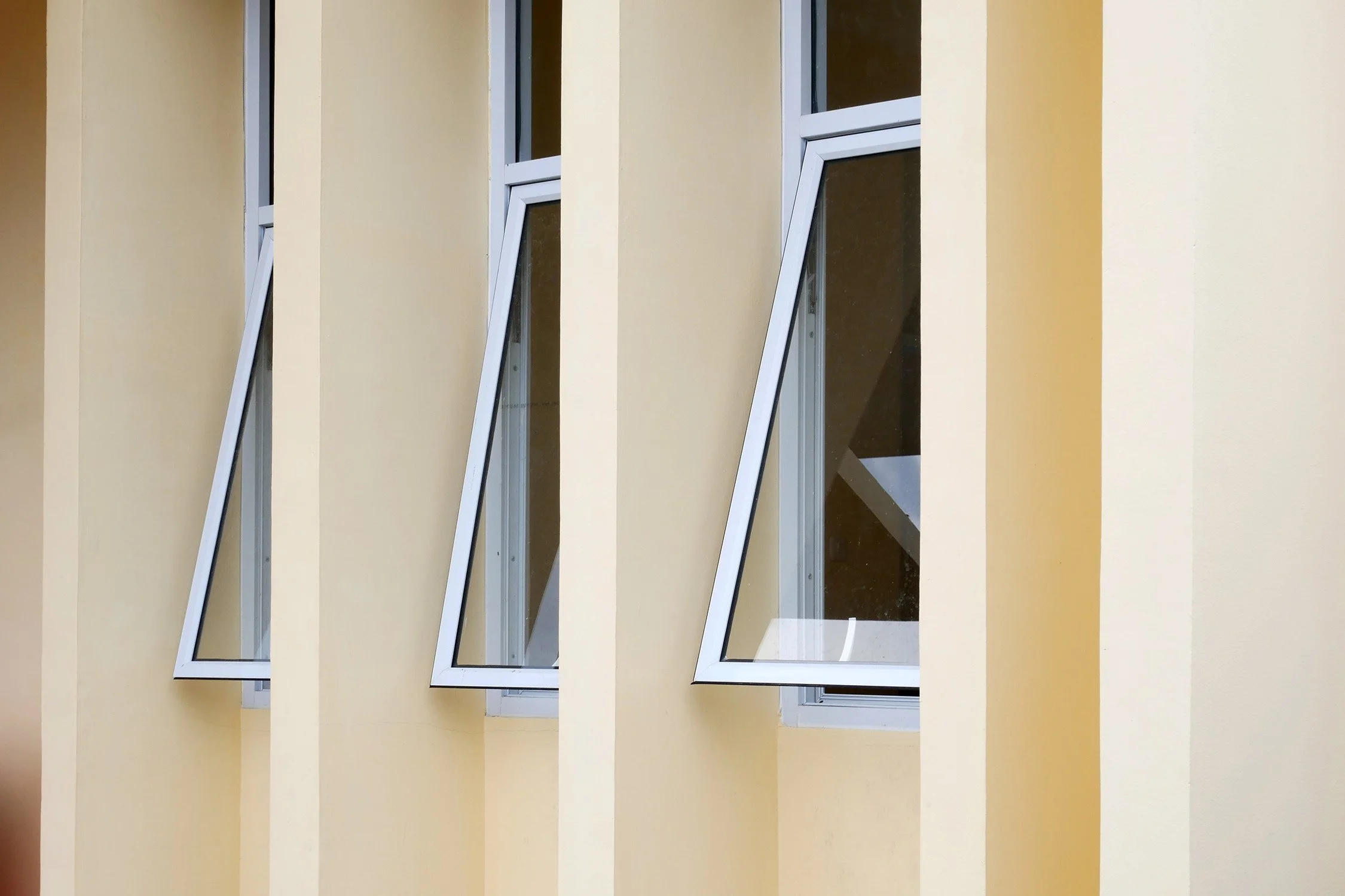 Three tall and narrow awning windows next to each other, separated by square pillars embedded into a wall.
