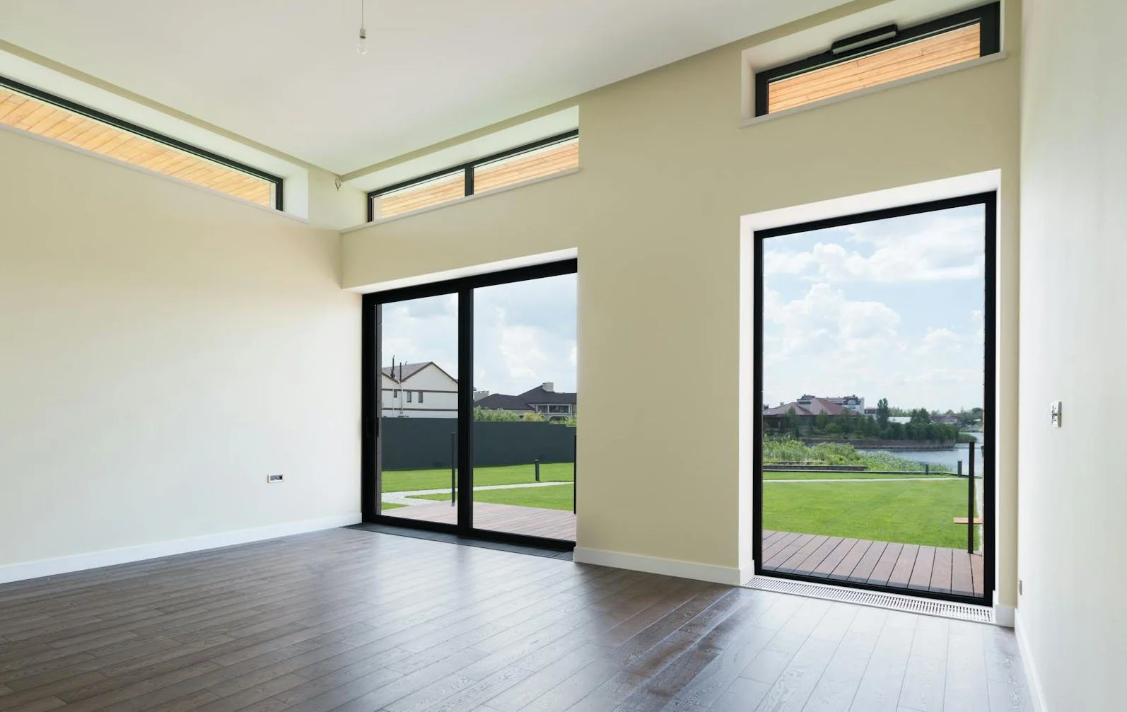Empty room with large black-framed, uPVC windows and doors looking out at green grass and a lake.