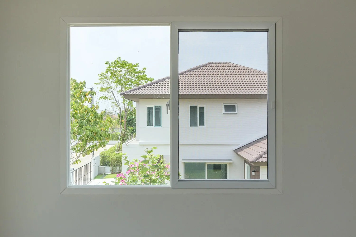 A view looking out of an open, white-framed, second-story window in an affluent neighborhood.