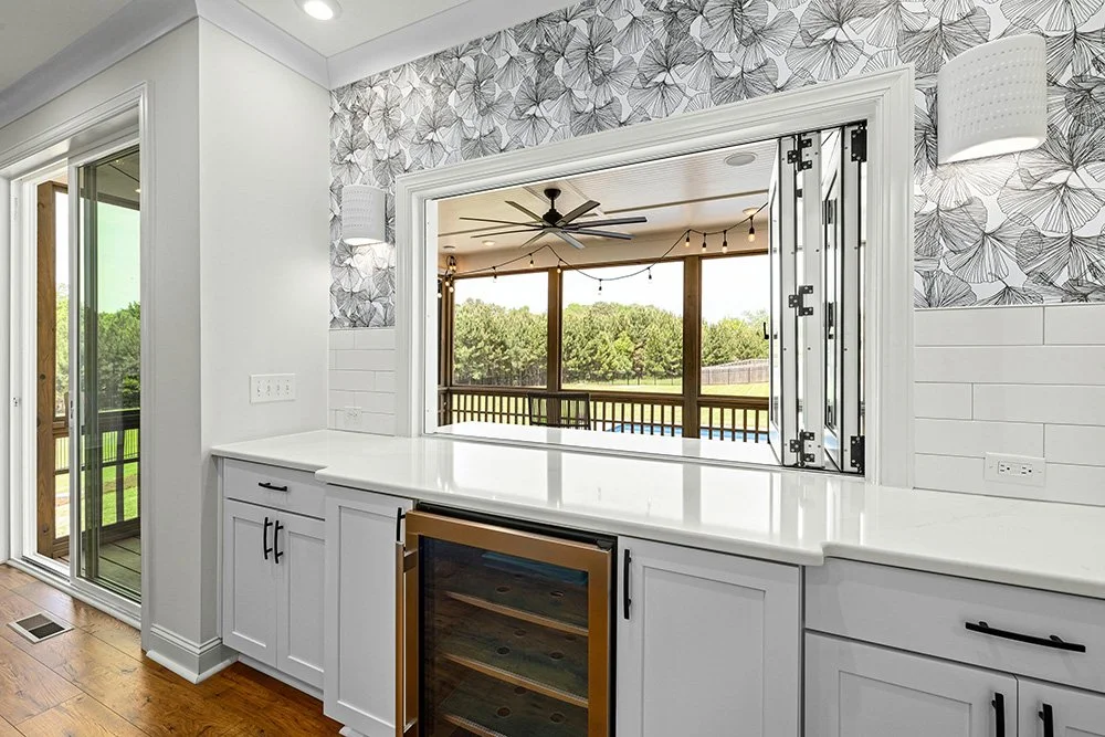 Stylish kitchen with a white-framed, three-panel bi-fold window that looks out onto a covered patio and of very large, grassy backyard.